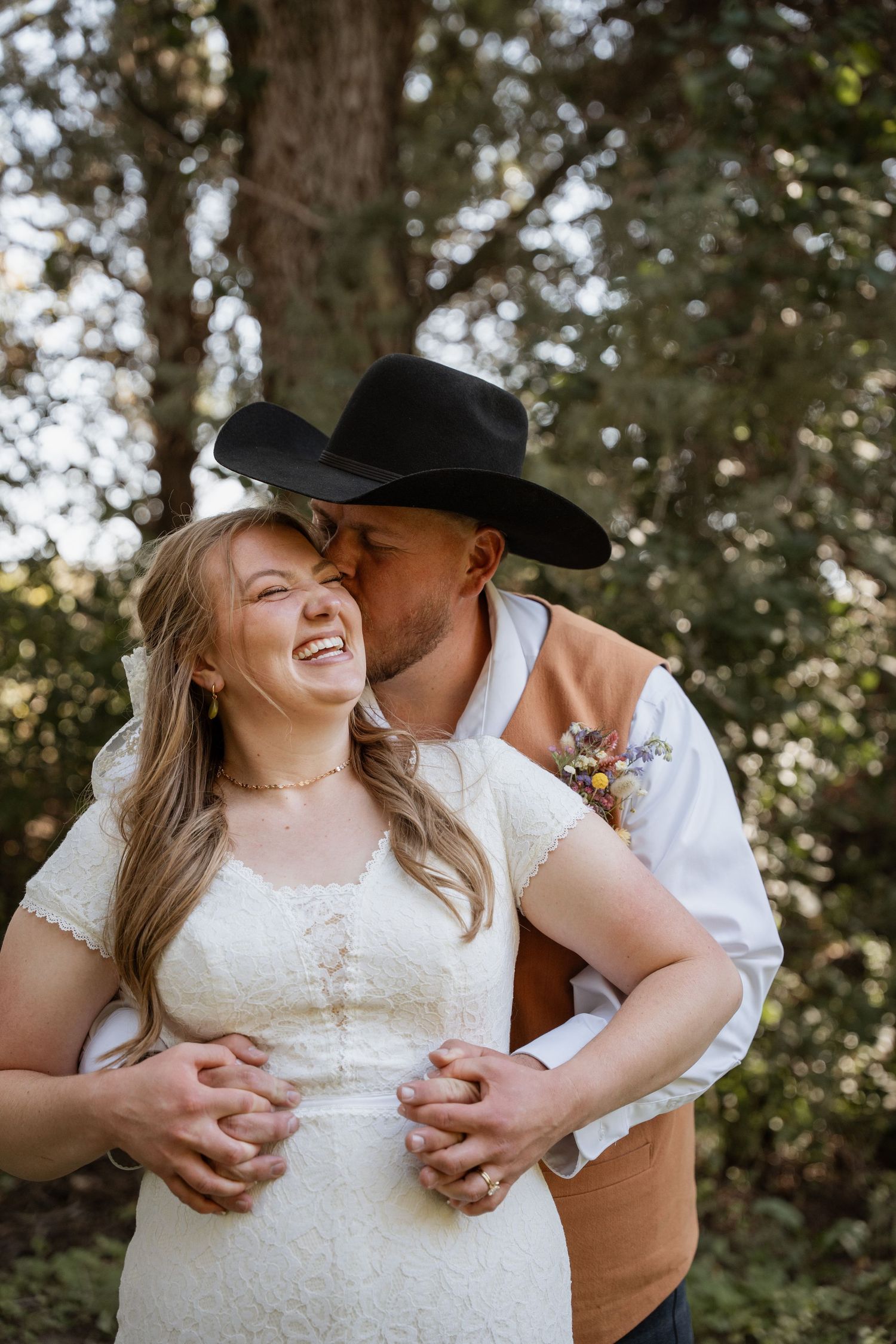 Des Moines Iowa wedding photographer – romantic forest portrait of bride and cowboy-hat groom sharing intimate kiss among trees.