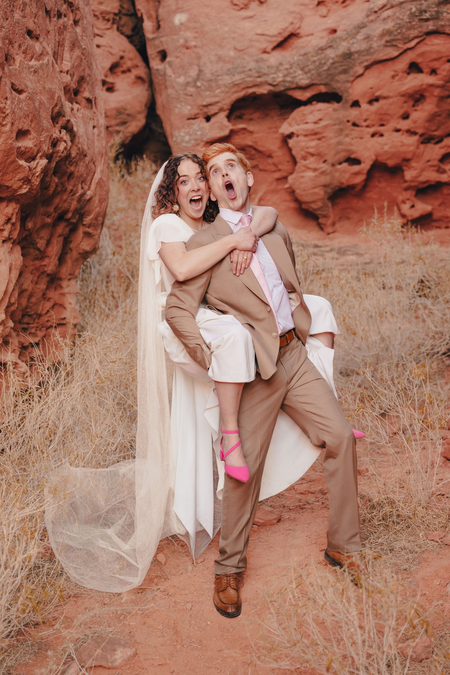 Bride and groom embracing in a red rock slot canyon during a romantic destination wedding portrait.