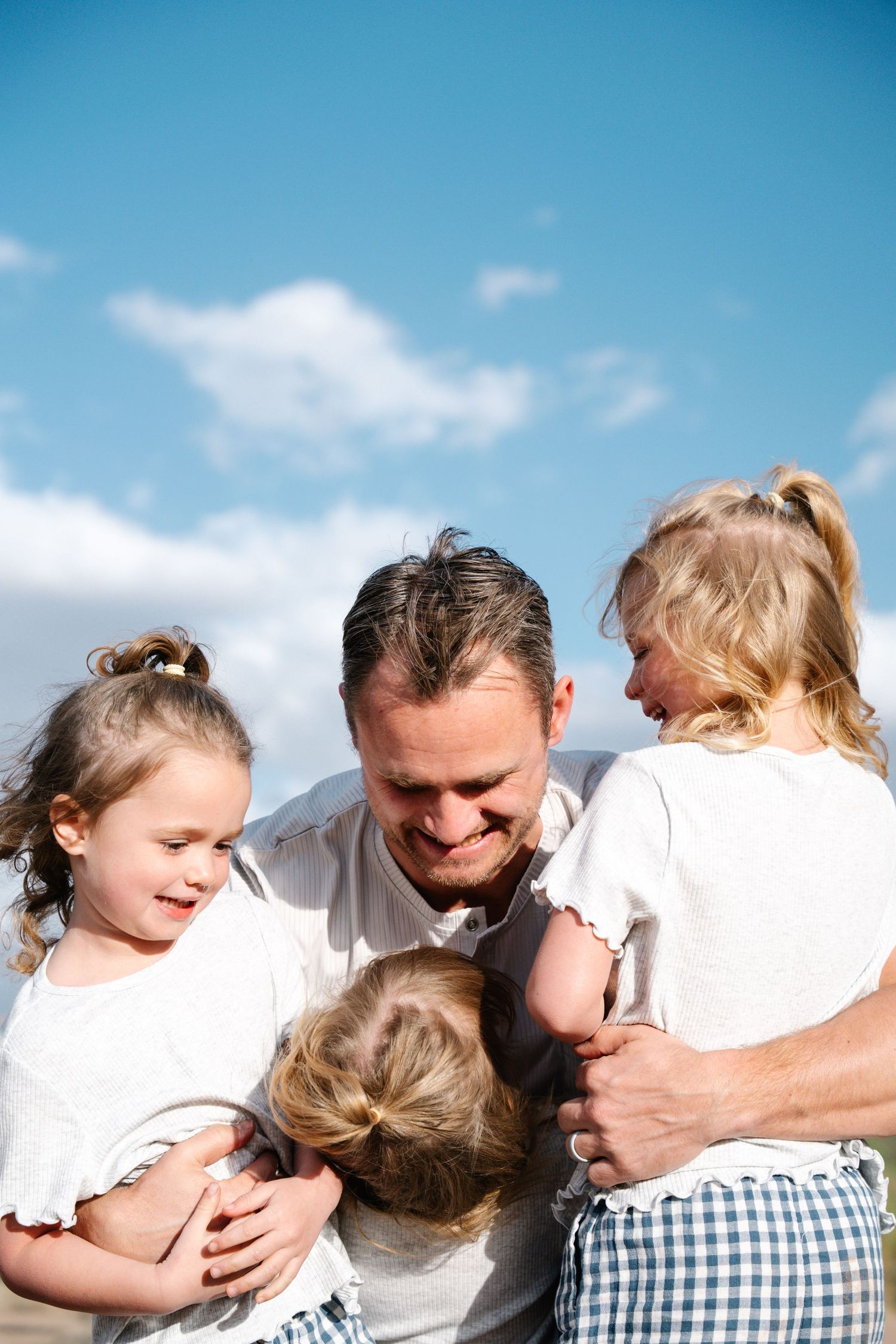 Des Moines Iowa family photographer – tender father-daughters group hug outdoors, loving embrace with three young girls in white dresses, he