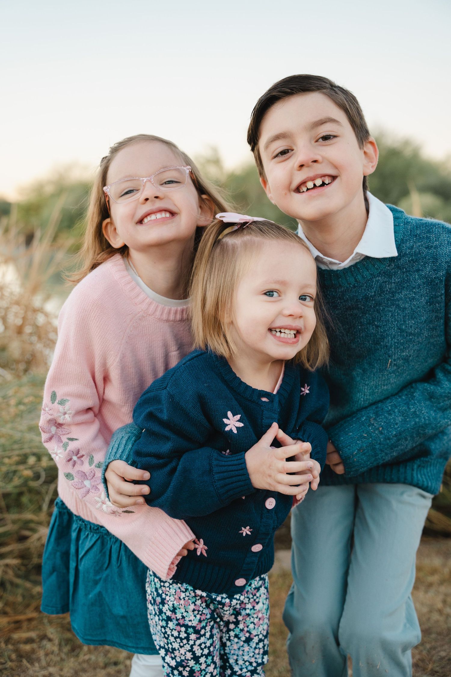 Des Moines Iowa lakeside family photographer – relaxed portrait of parents and three kids smiling together by the water, genuine family joy.