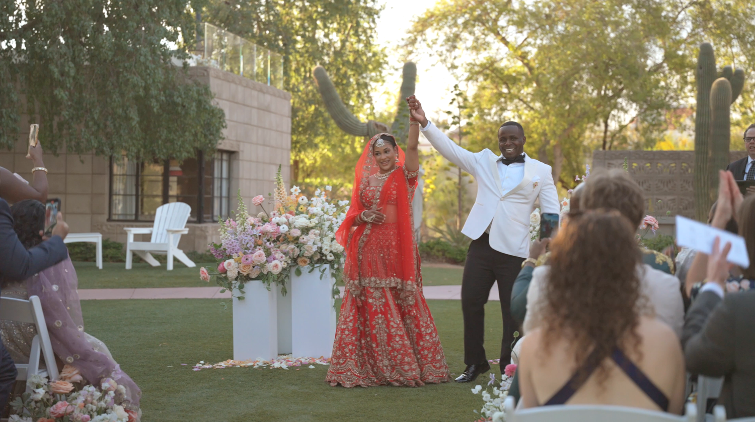 Des Moines Iowa wedding photographer – vibrant Indian fusion ceremony with bride in red lehenga raising hands in joy, groom beside her.