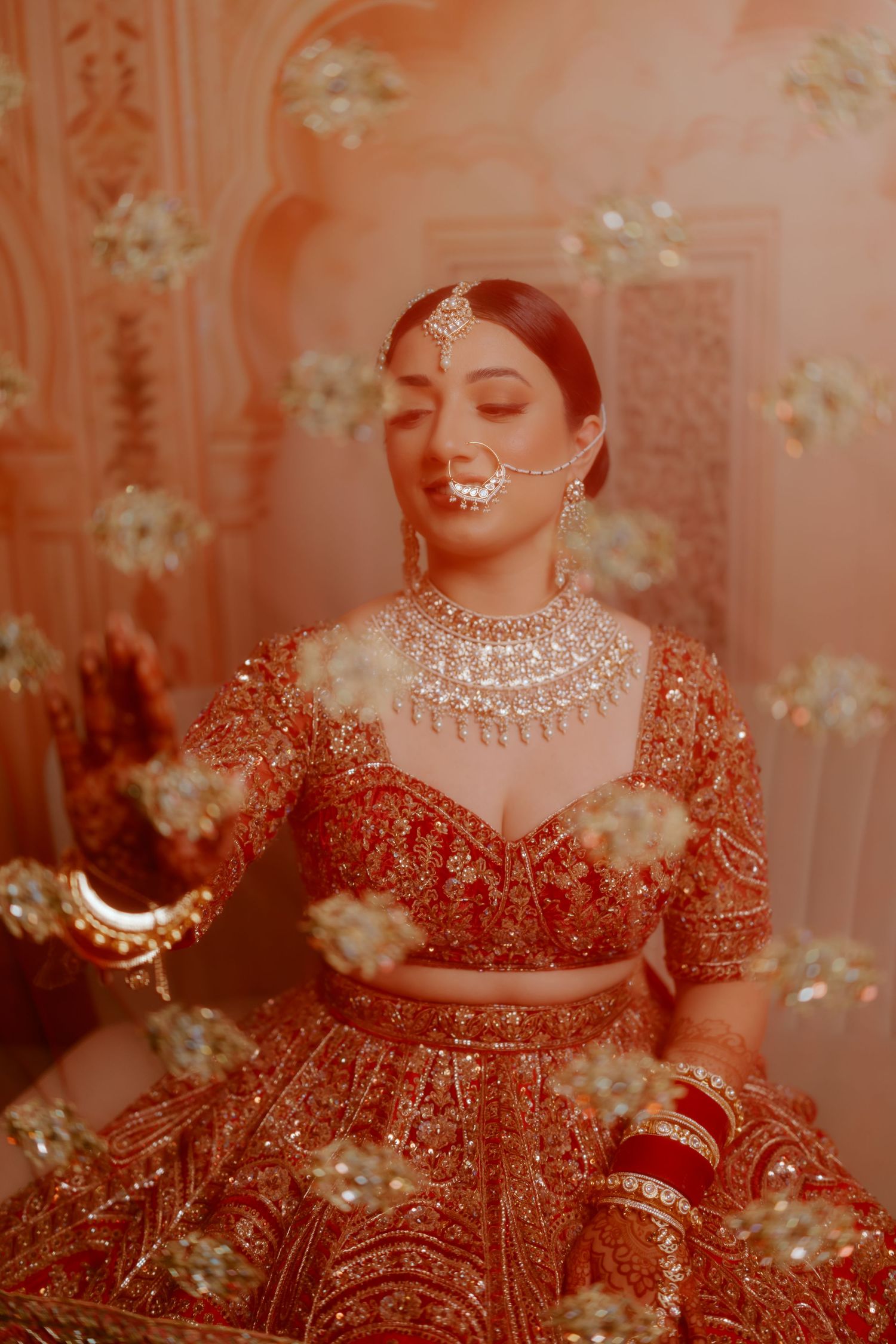 Traditional Indian bridal portrait showing intricate red lehenga and statement pearl jewelry against a peachy backdrop.
Bridal portraits