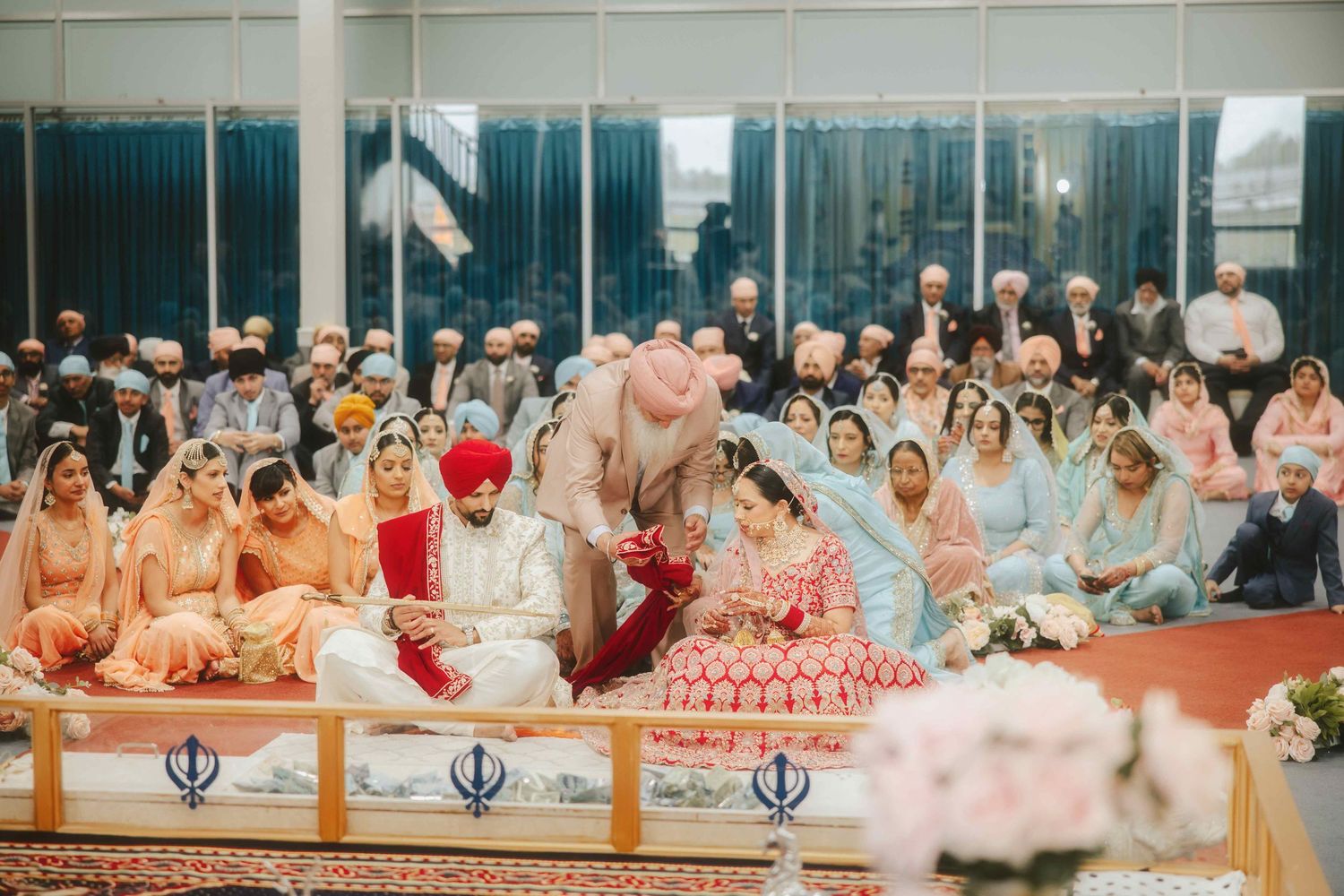 Large group attending traditional Sikh wedding ceremony with couple in ornate traditional dress.
Anand Karaj