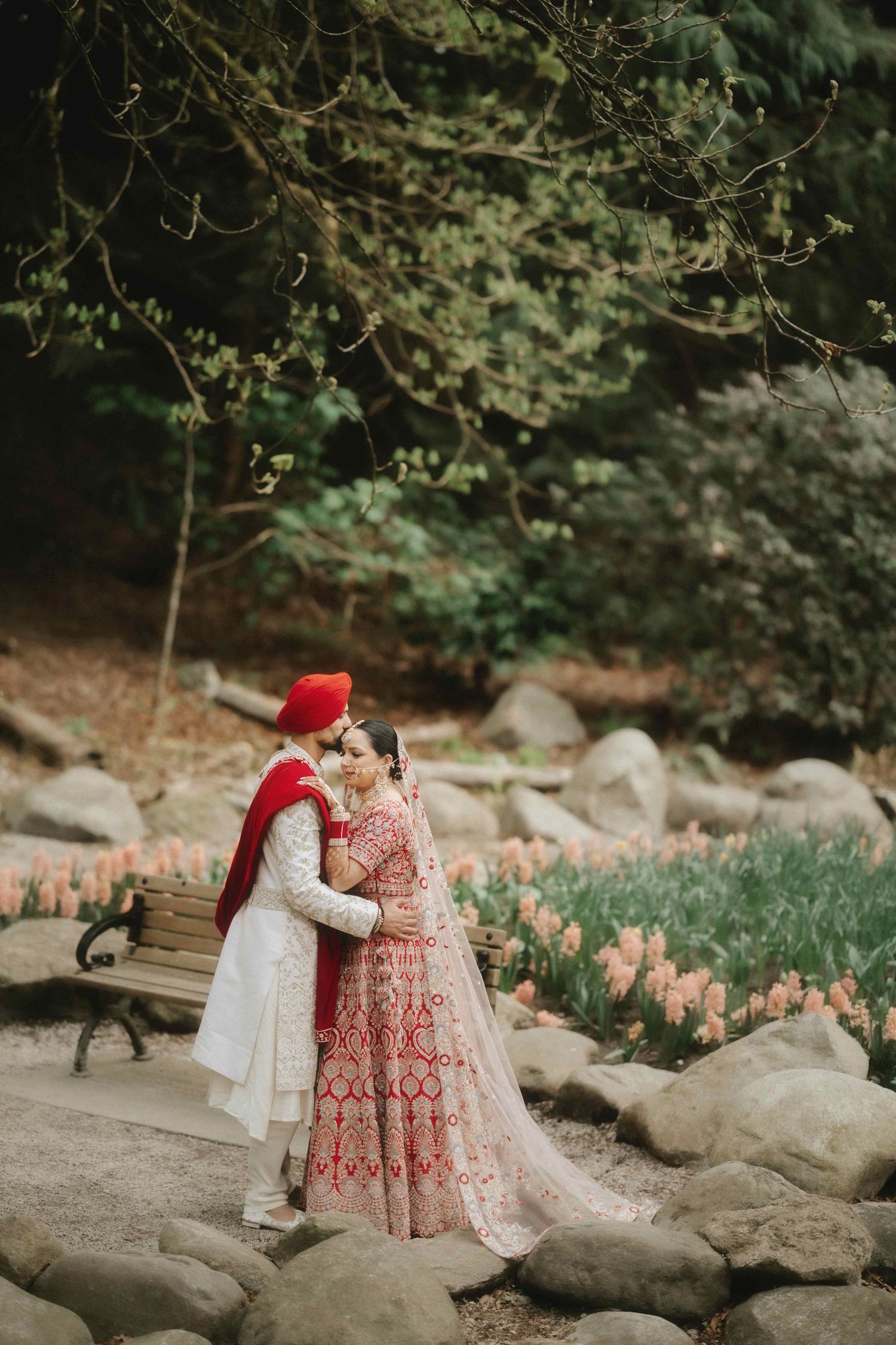 Romantic couple in traditional Indian wedding attire embracing near blooming tulips and rocks in a garden.
Vancouver Wedding Photographer