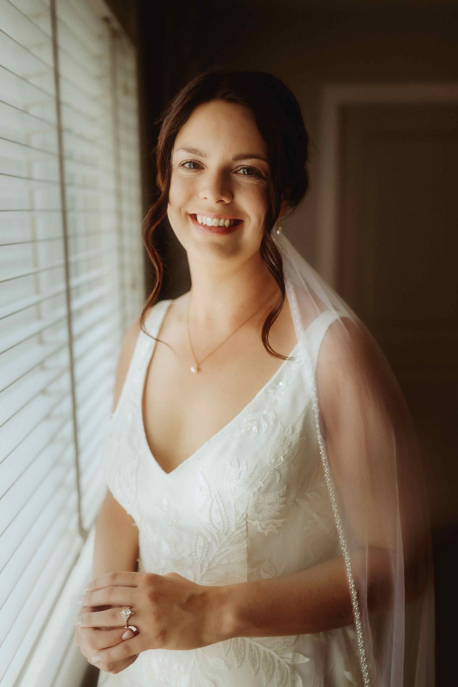 Elegant white lace wedding dress detail shot near a window with soft natural lighting.
White wedding