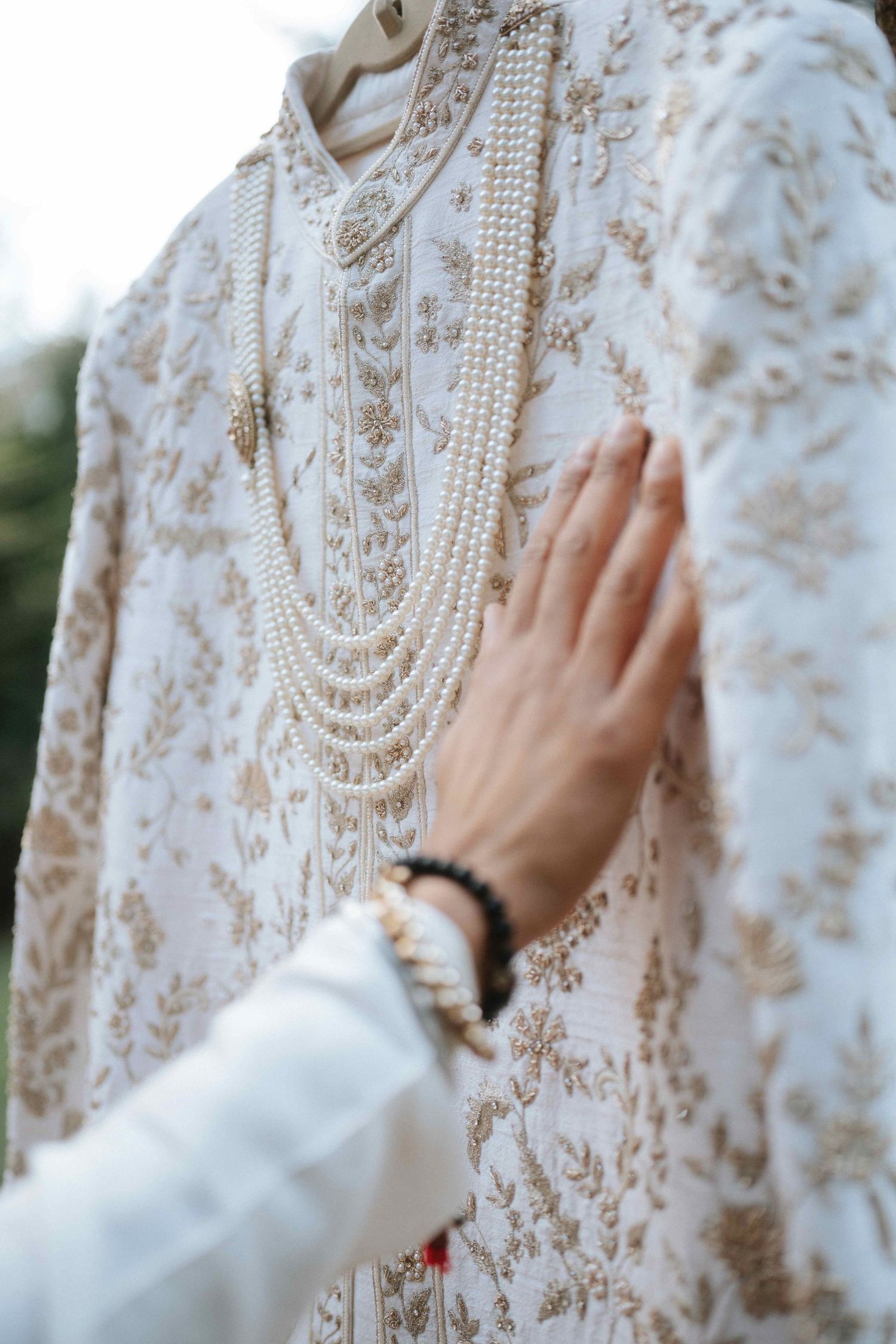 Close-up of intricate white embroidery and pearl details on traditional wedding attire.
Groom portrait photography