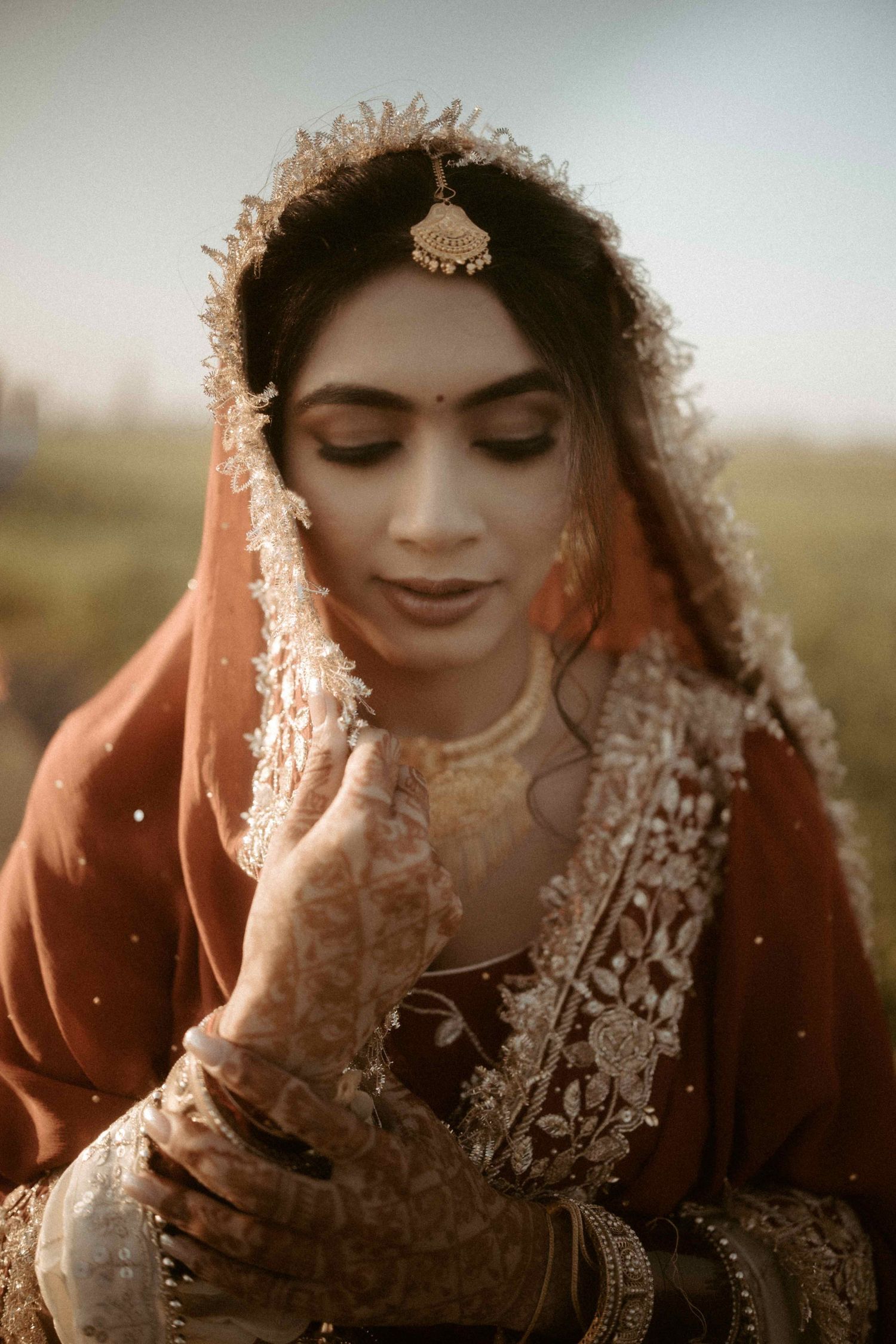 Traditional South Asian bride in orange dupatta with intricate henna and jewelry in warm sunset lighting.
Punjabi bride