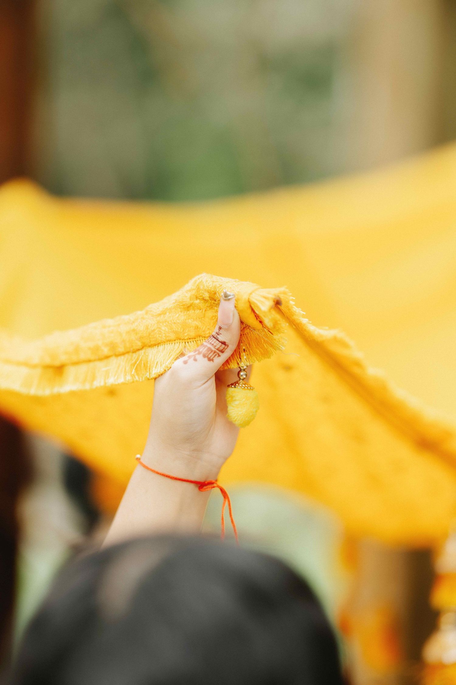 A hand with a red string bracelet holds a yellow fabric in natural lighting.
Haldi Ceremony