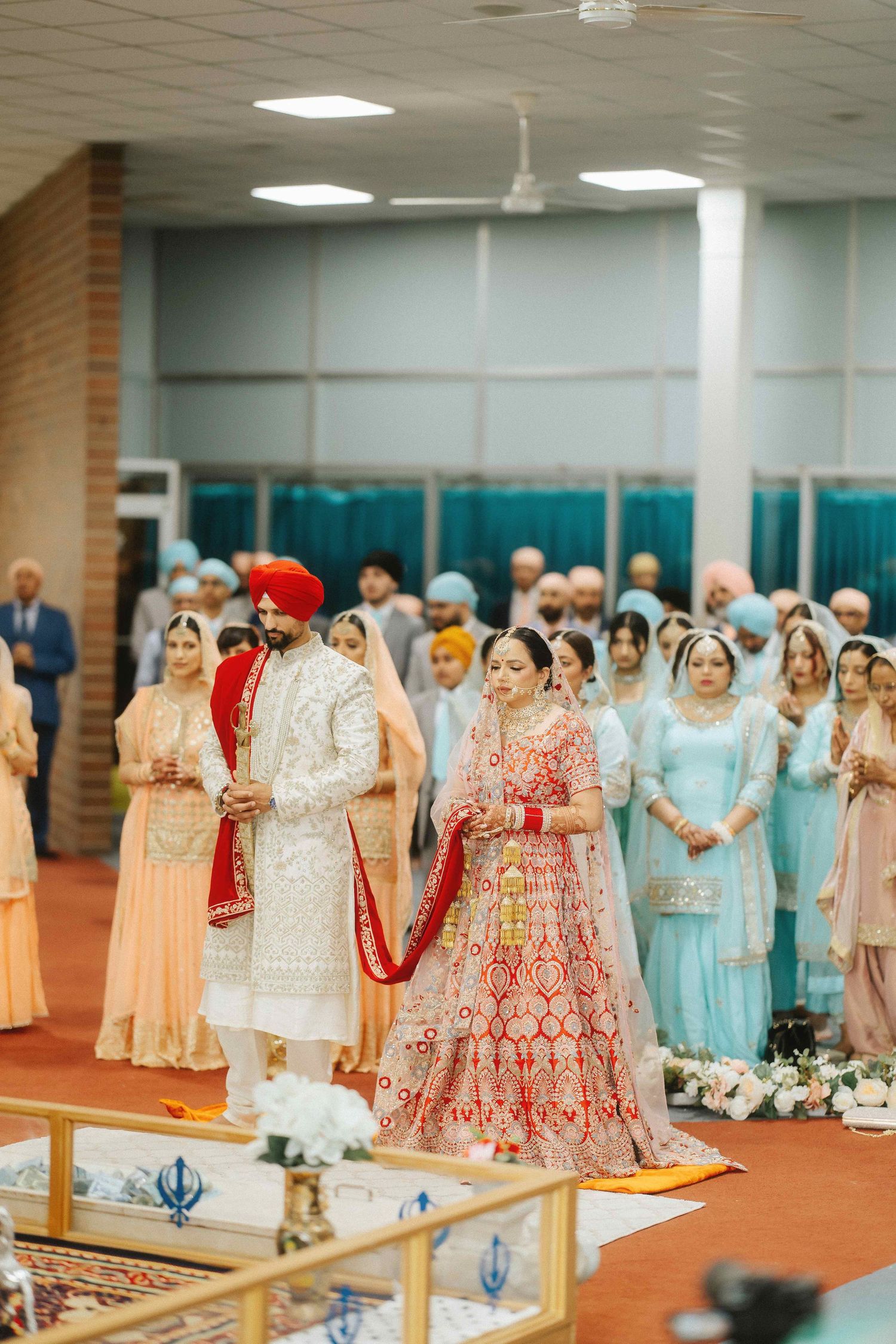Traditional Sikh wedding ceremony taking place in a spacious indoor venue with guests seated on the floor.
Anand Karaj