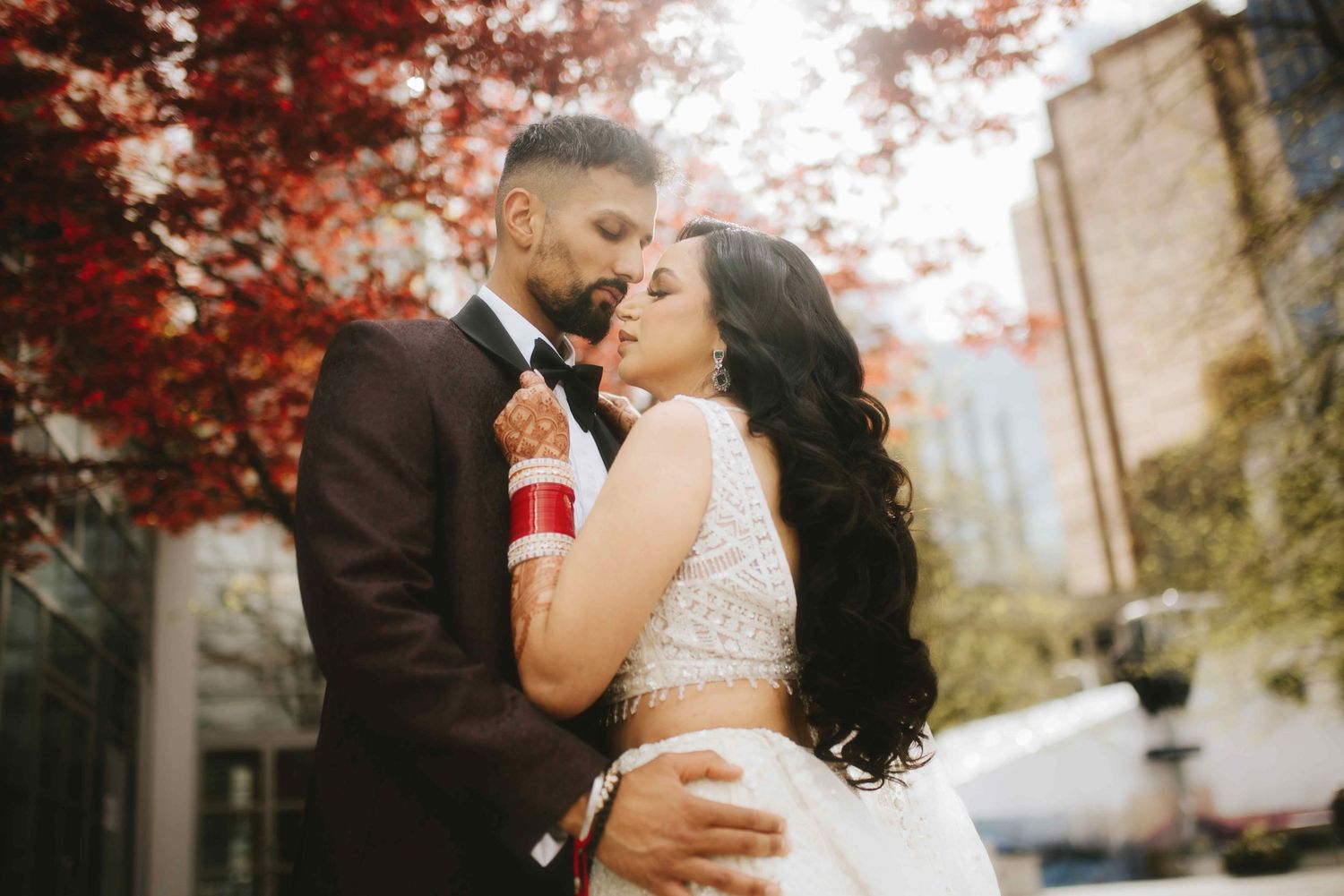 Romantic urban wedding photo with couple embracing under red autumn trees.