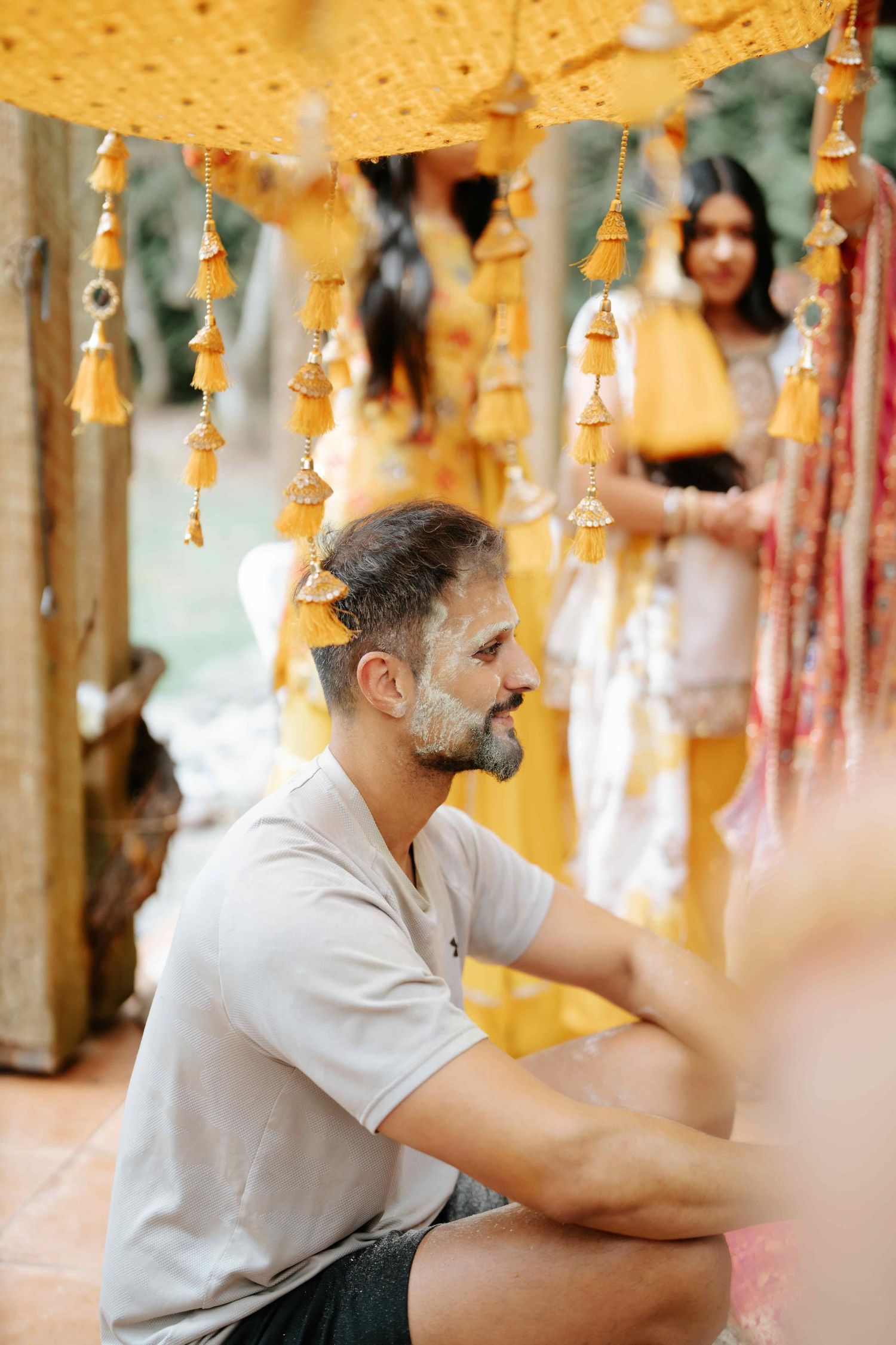 A candid shot under warm yellow lighting with hanging decorative elements in the background.
Vatna Ceremony
