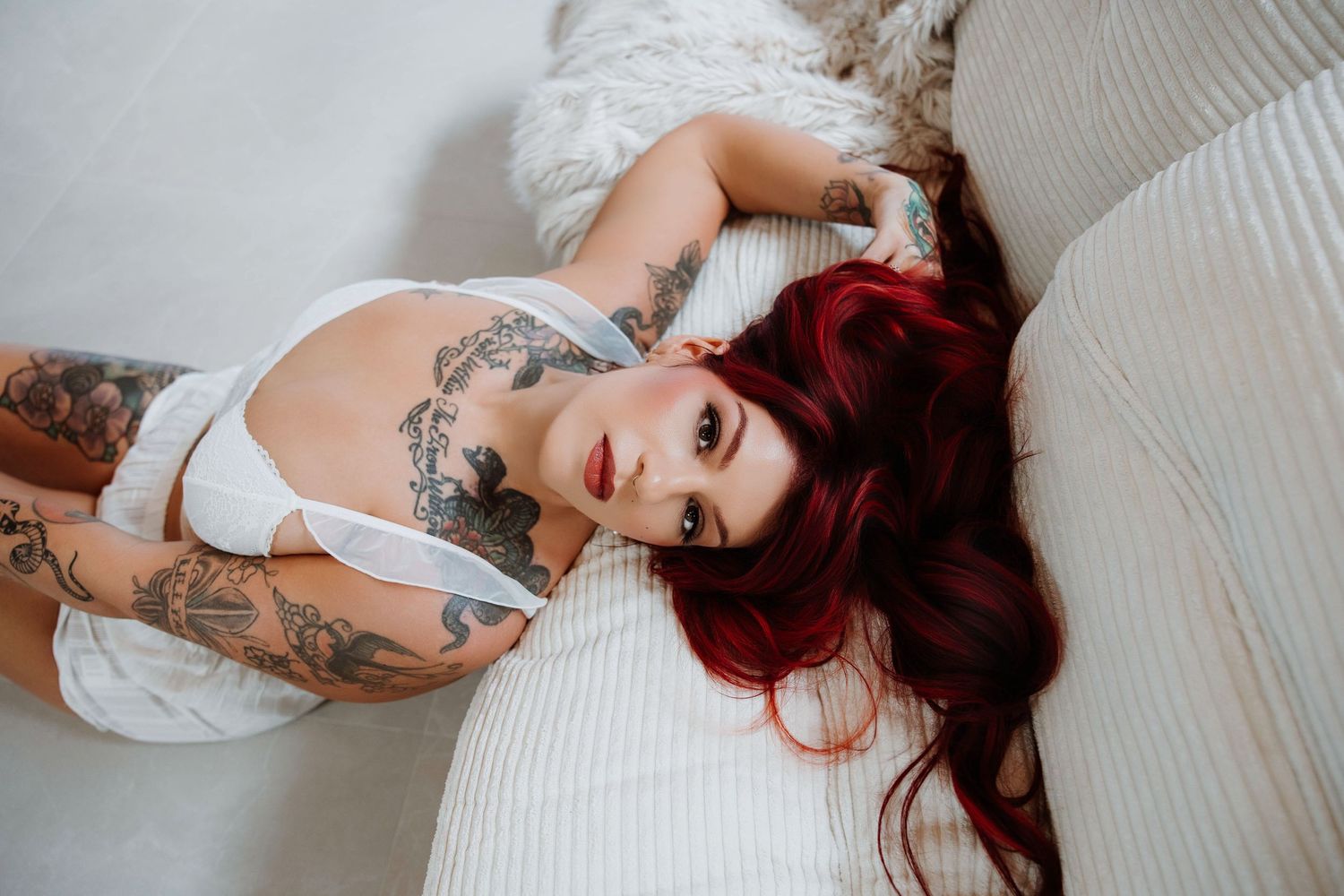 Tattooed woman reclined in a white lingerie durning an intimate portrait session