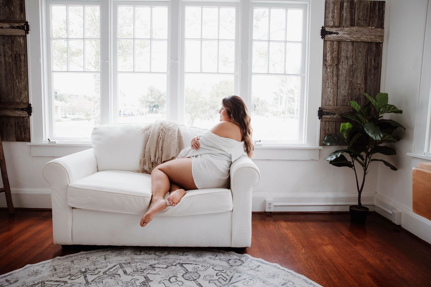 Woman sitting on a couch looking out the window durning an in home boudoir session