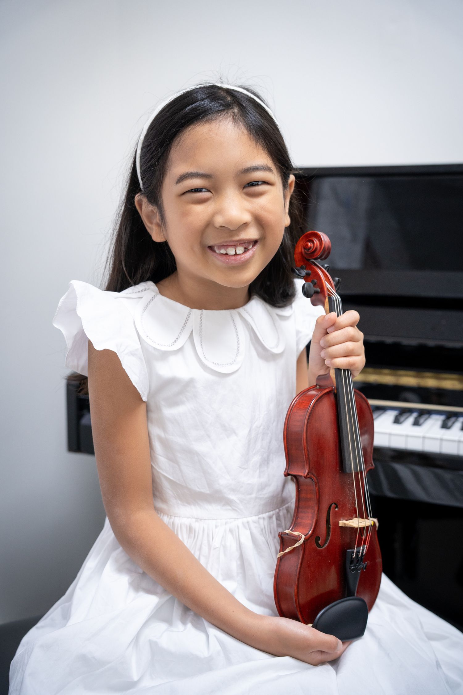 Portrait of a smiling young girl in a white dress holding her violin.