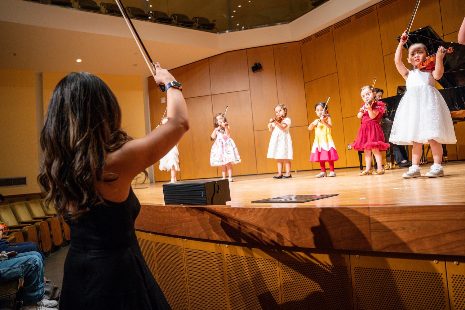 Music teacher conducting a group of young violinists on stage.