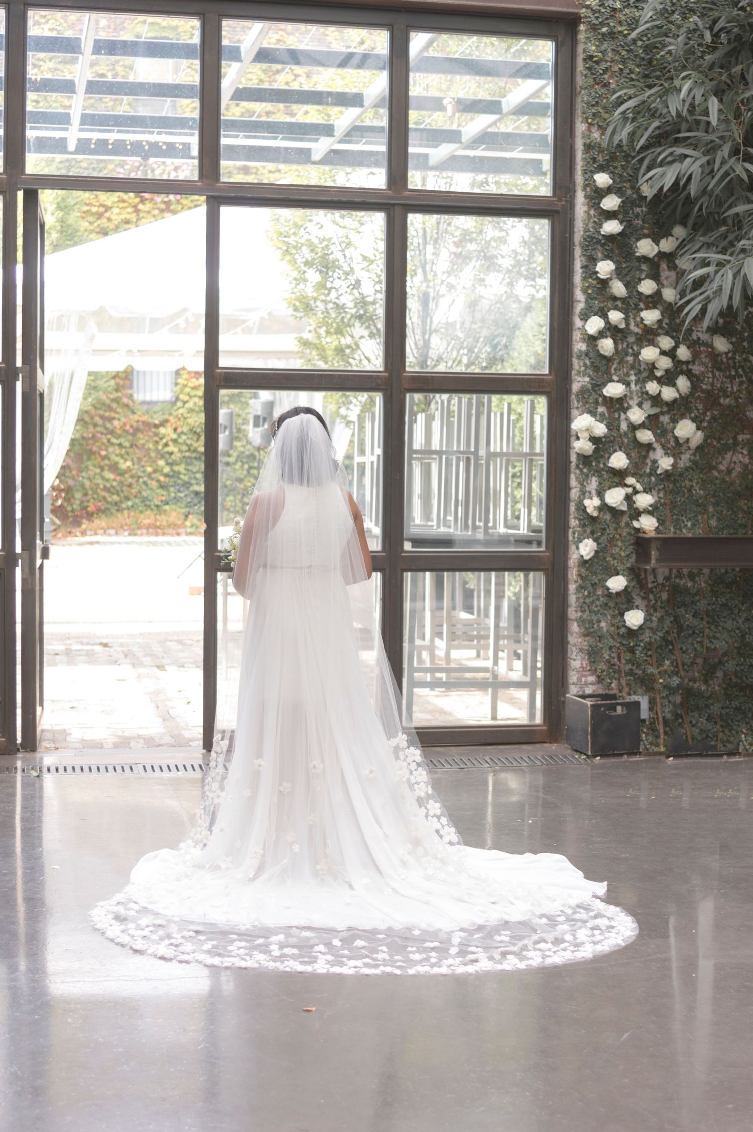 Bride in a lace wedding gown posing in front of a large sunlit window.
