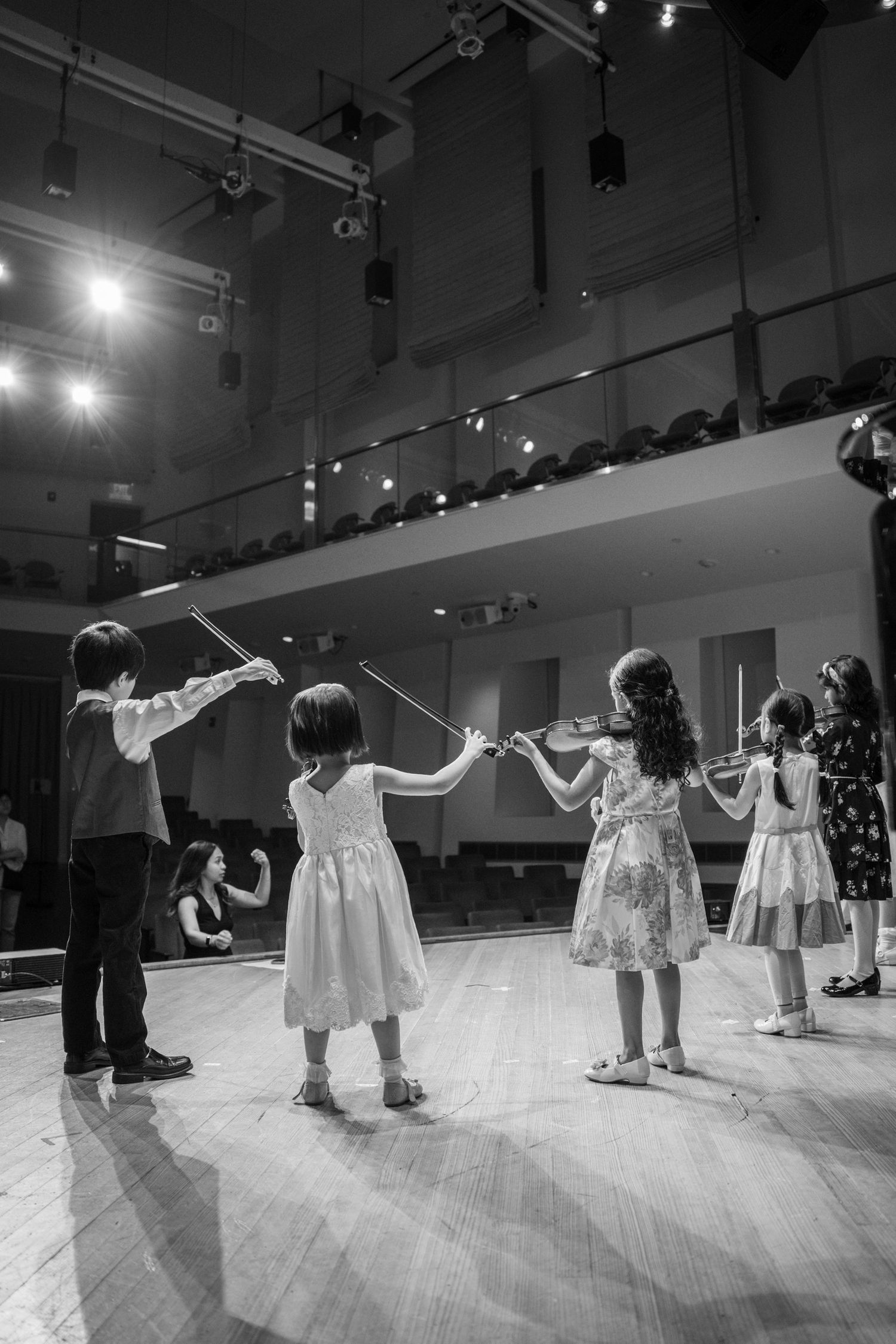 Children standing on stage during a music recital, captured in black and white.