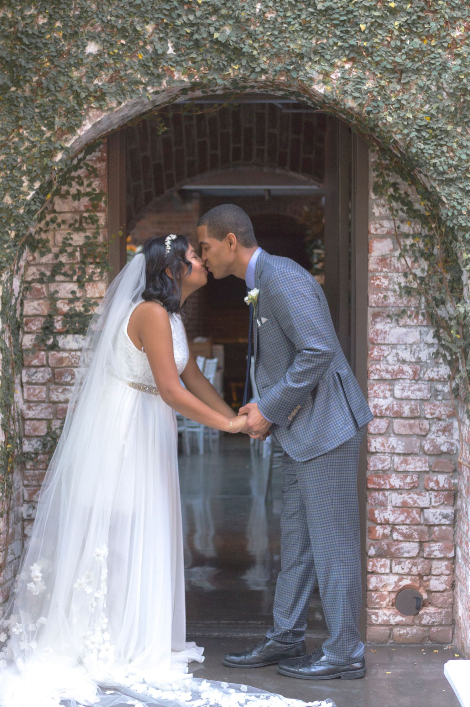 Bride and groom kissing under a rustic brick archway.