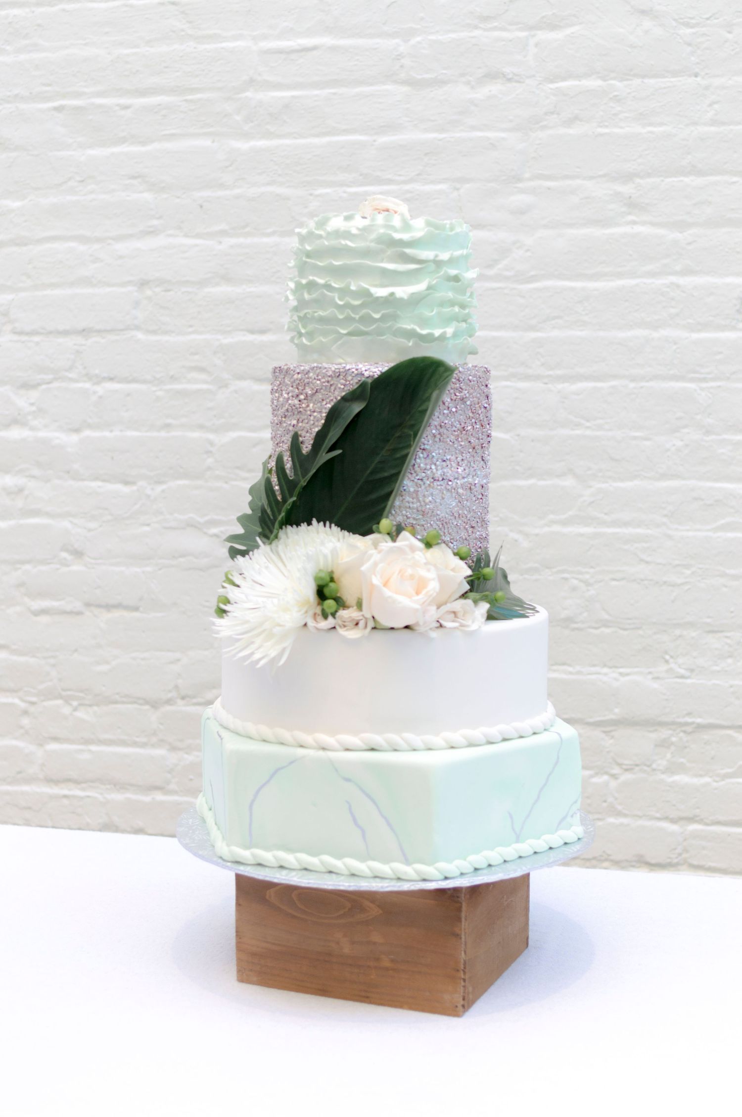 Pastel-colored tiered wedding cake decorated with flowers and green leaves.