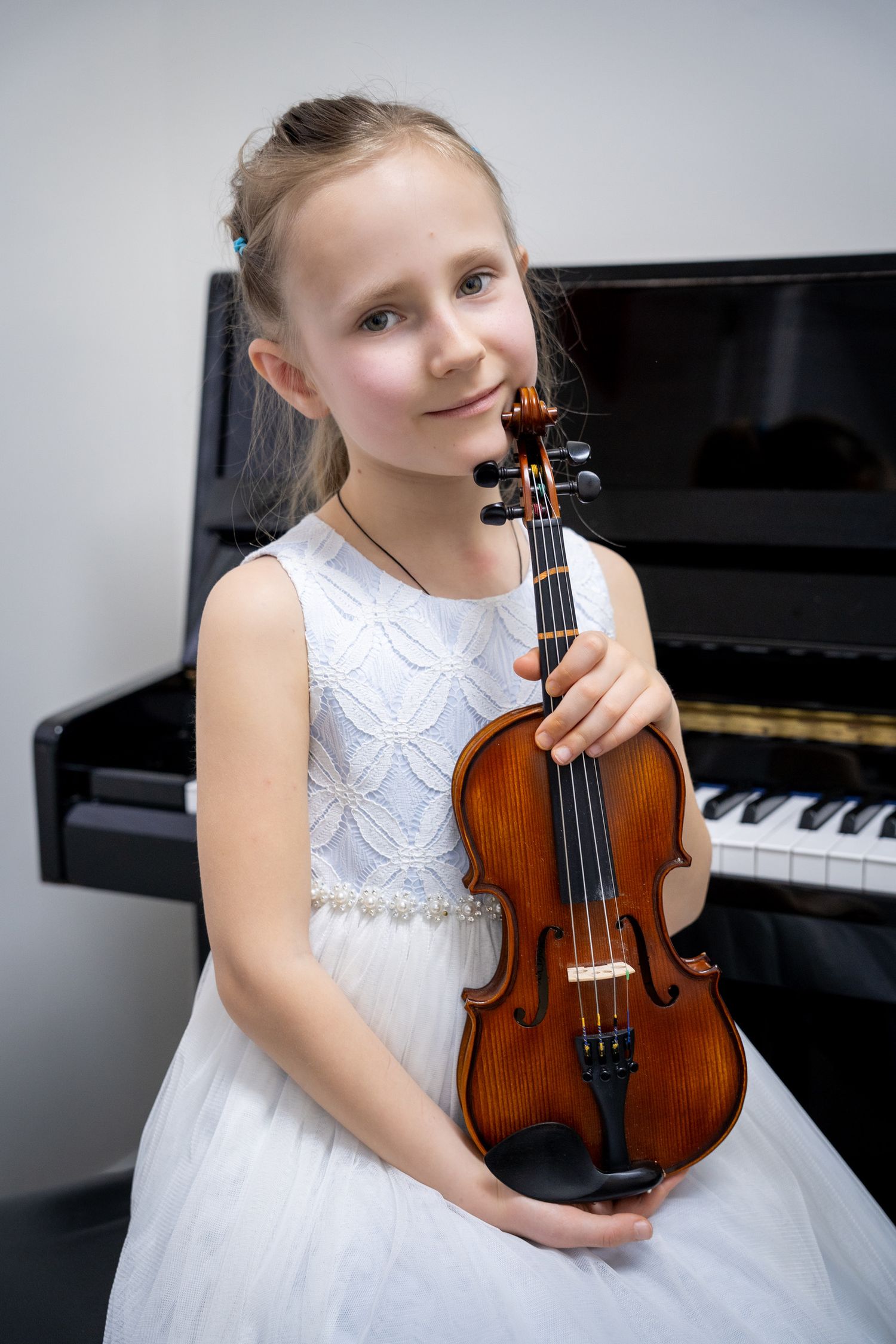 Portrait of a young girl in a white dress smiling and holding her violin.
