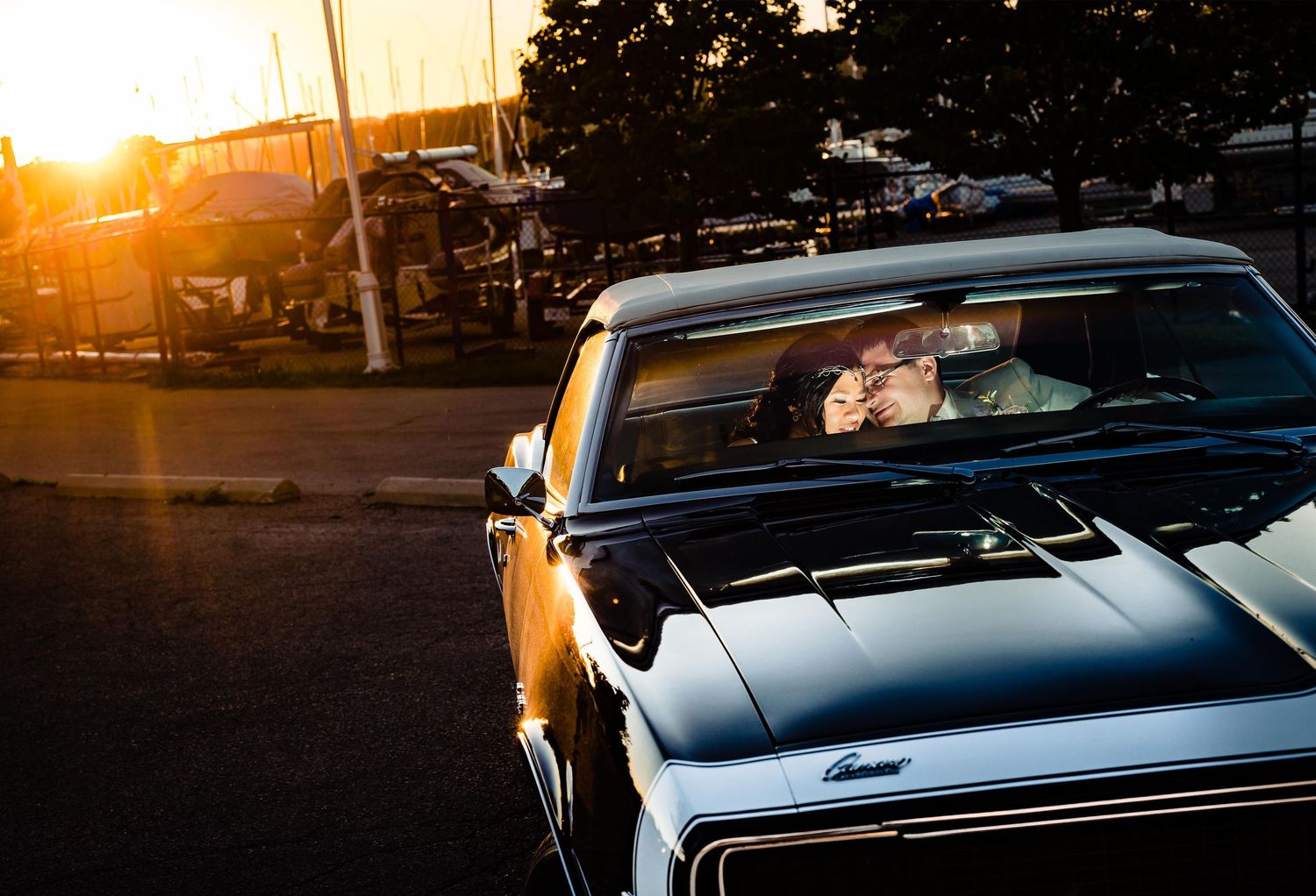Classic car silhouetted against golden sunset light in parking area with warm evening glow.