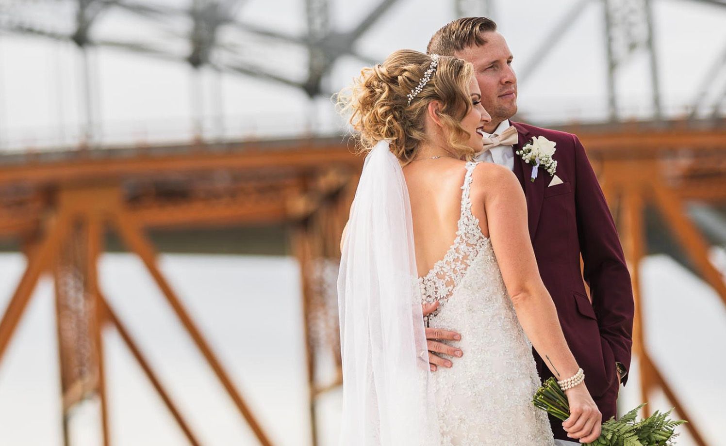A bride and groom share a romantic moment together on a bridge with rustic steel beams in the background.