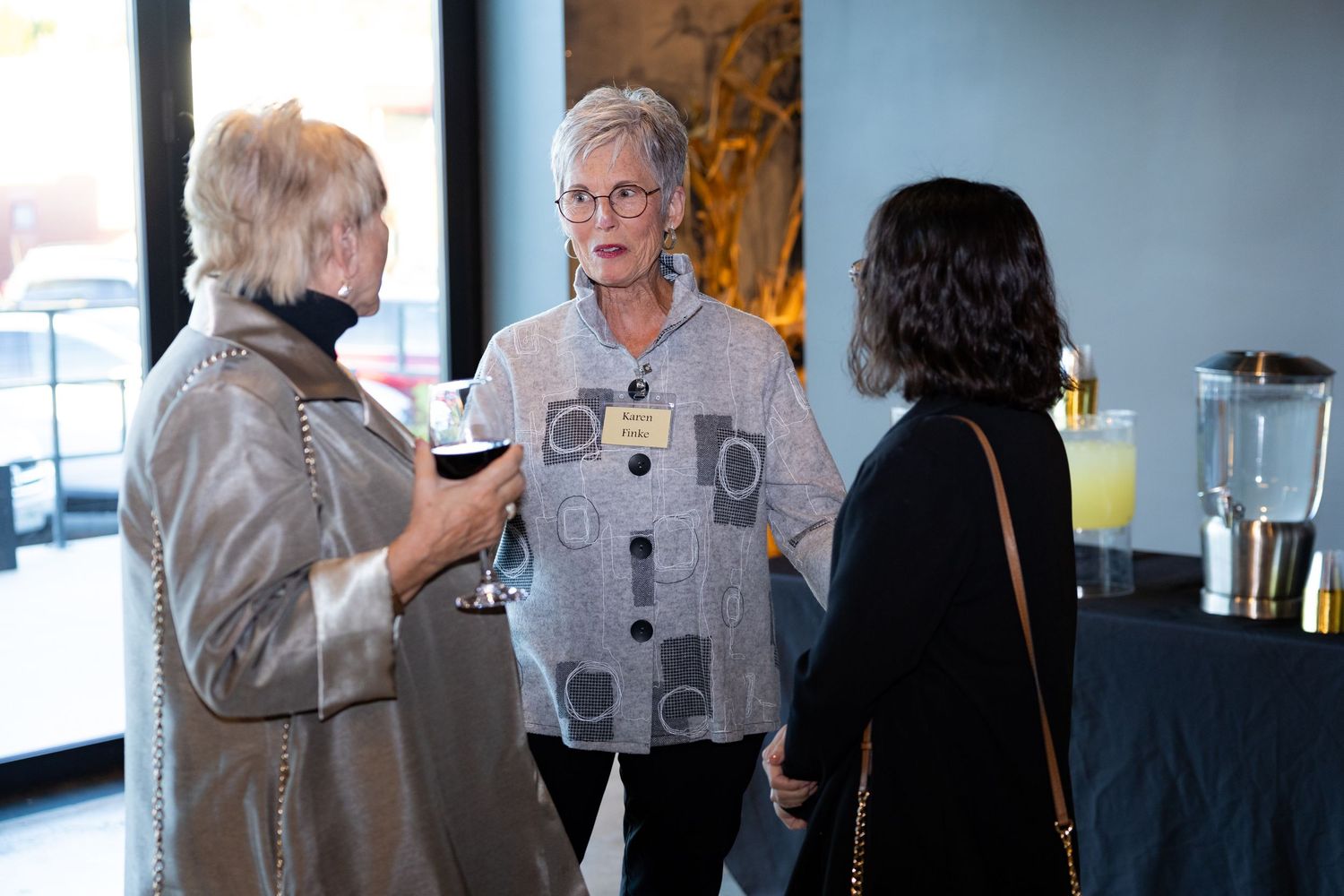 Three women networking at an indoor cocktail reception, one holding a glass of red wine.