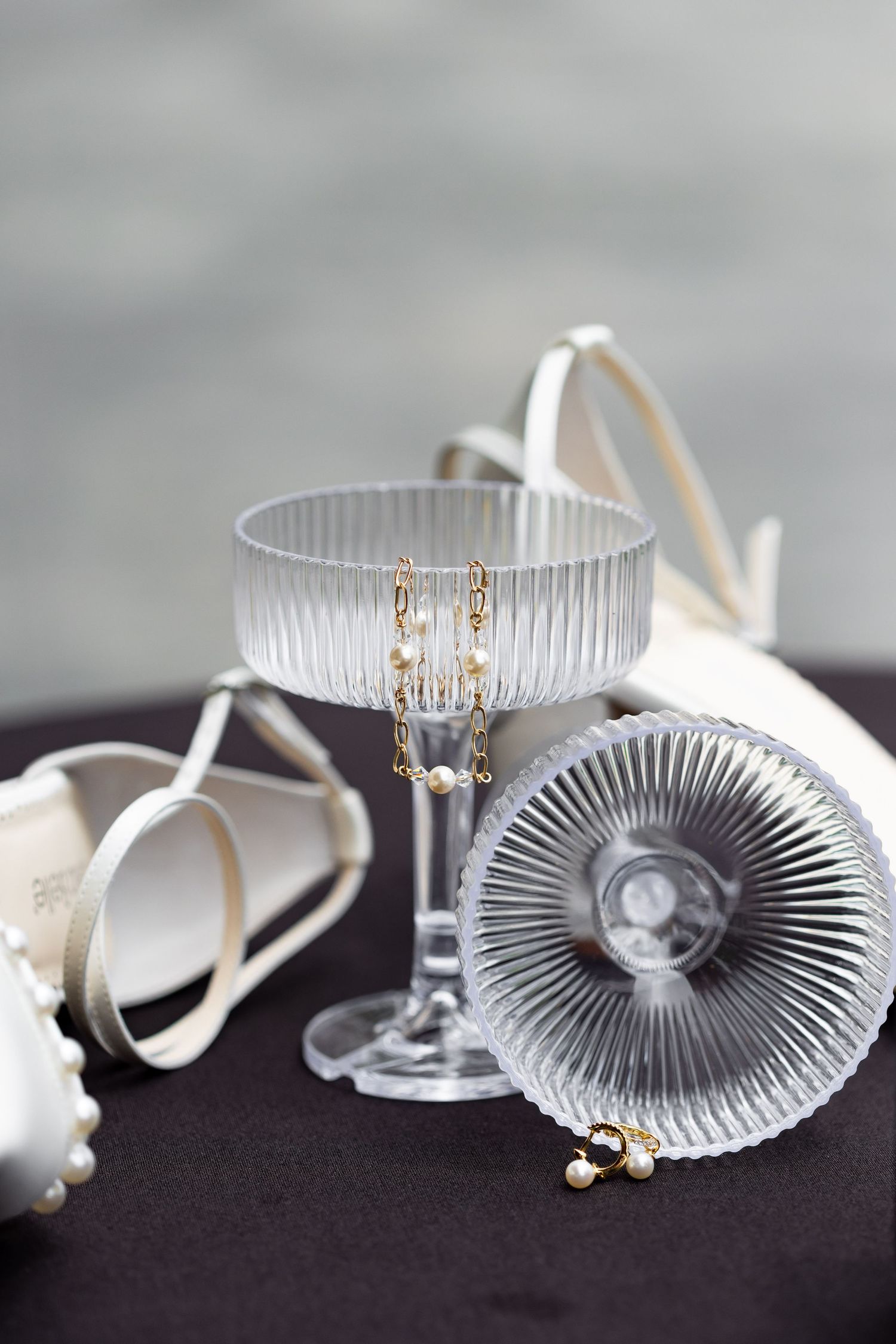Elegant bridal jewelry displayed in crystal glasses with white heels on dark surface.