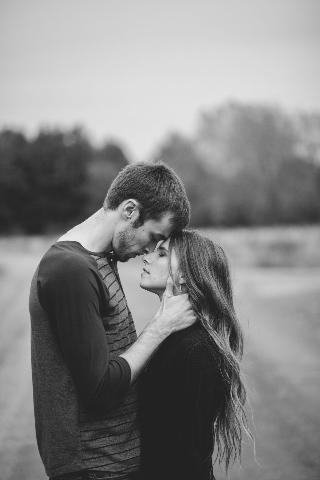 Black and white photo of a romantic couple almost kissing outdoors in a field.