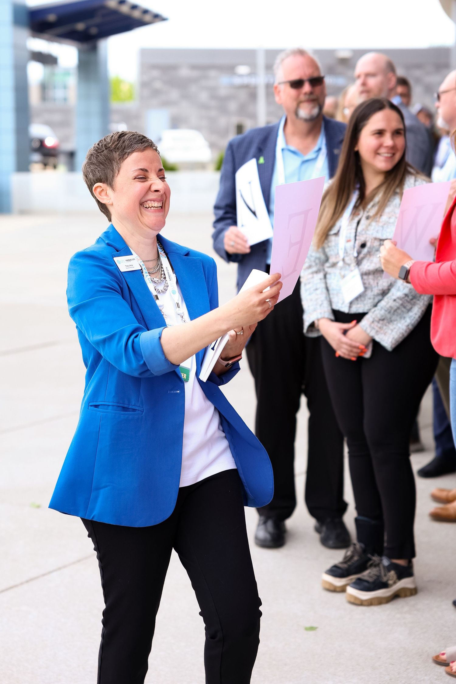 Woman in bright blue blazer laughing while holding papers outdoors at a professional group event.