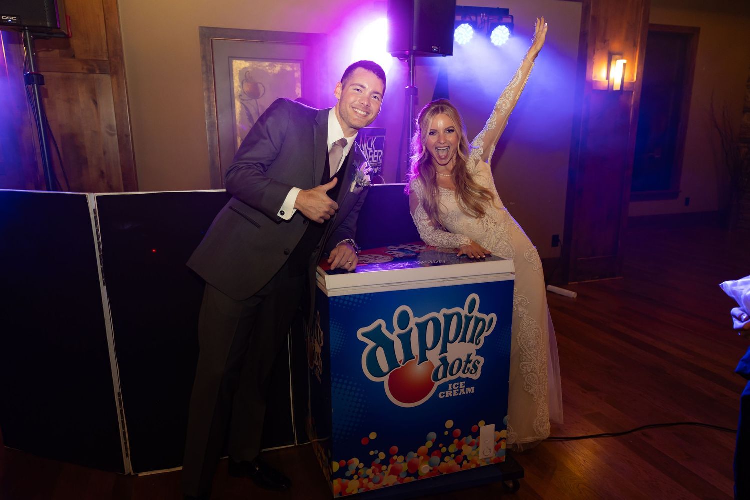 Smiling bride and groom pose beside Dippin Dots cart at festive wedding reception.