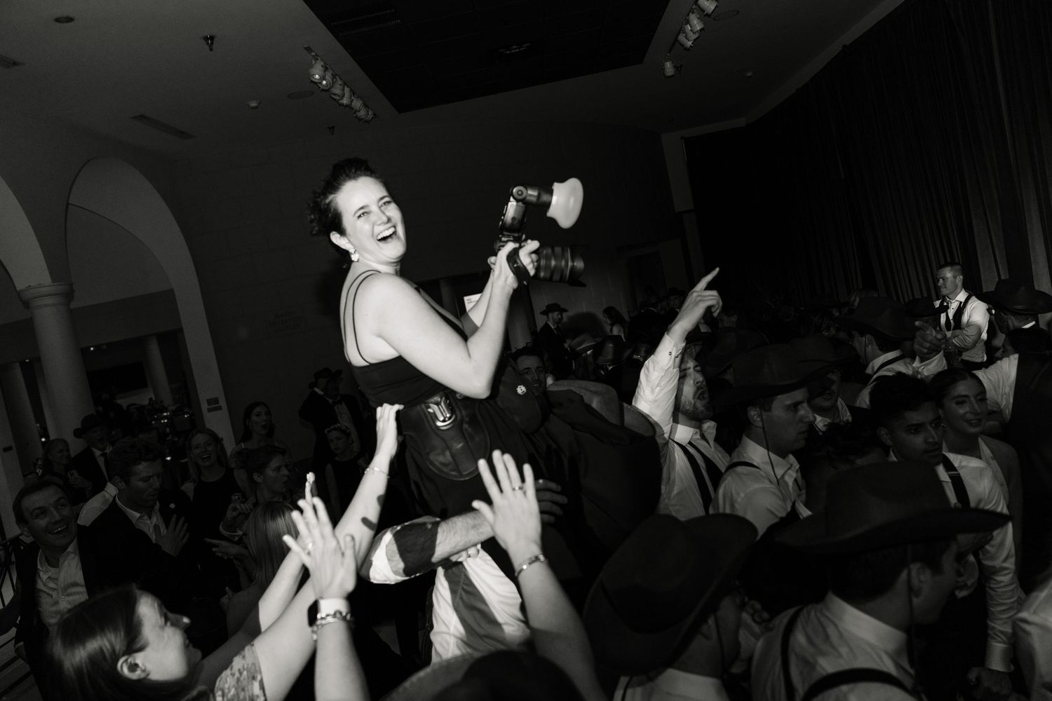 Black and white photo of a woman crowd surfing at a lively wedding reception party.