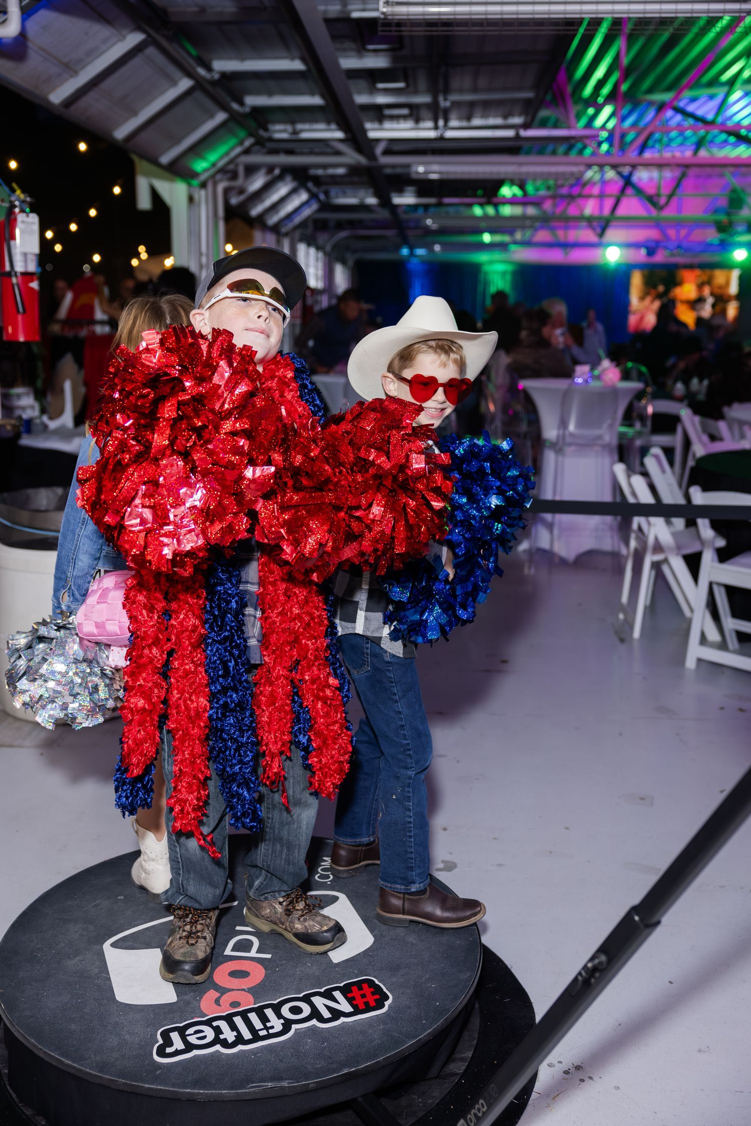 Two people in cowboy hats and red tinsel decorations pose at a western-themed party.
