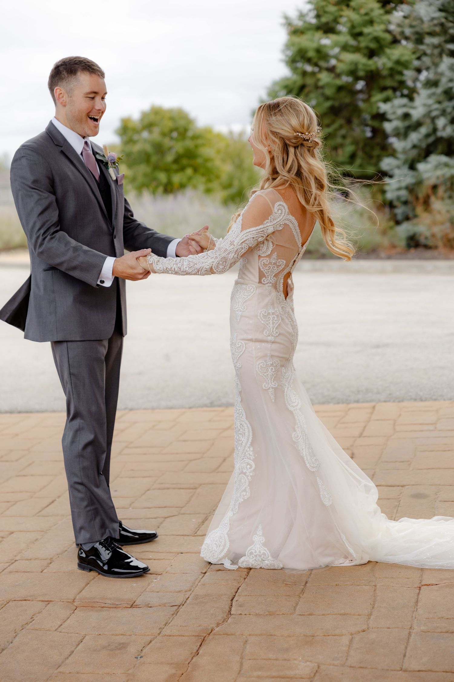 Groom laughing joyfully while holding bride's hands during first look at wedding.