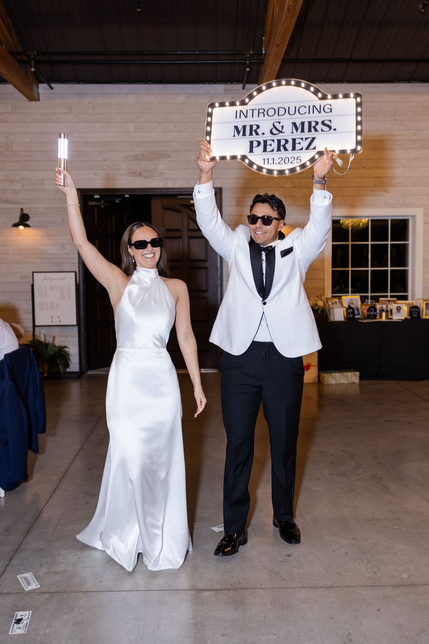 Newlyweds celebrating grand entrance holding illuminated Mr. and Mrs. Perez sign at wedding reception.