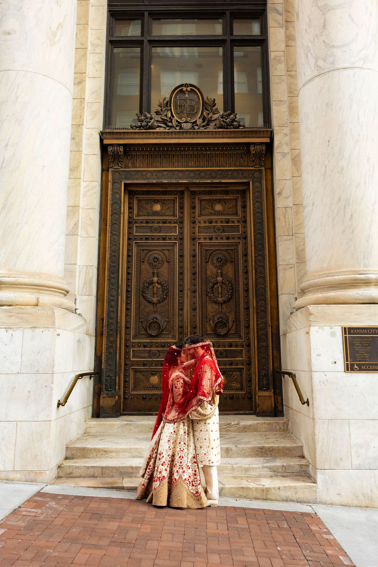 Indian bride and groom sharing a kiss in front of ornate bronze doors outdoors.