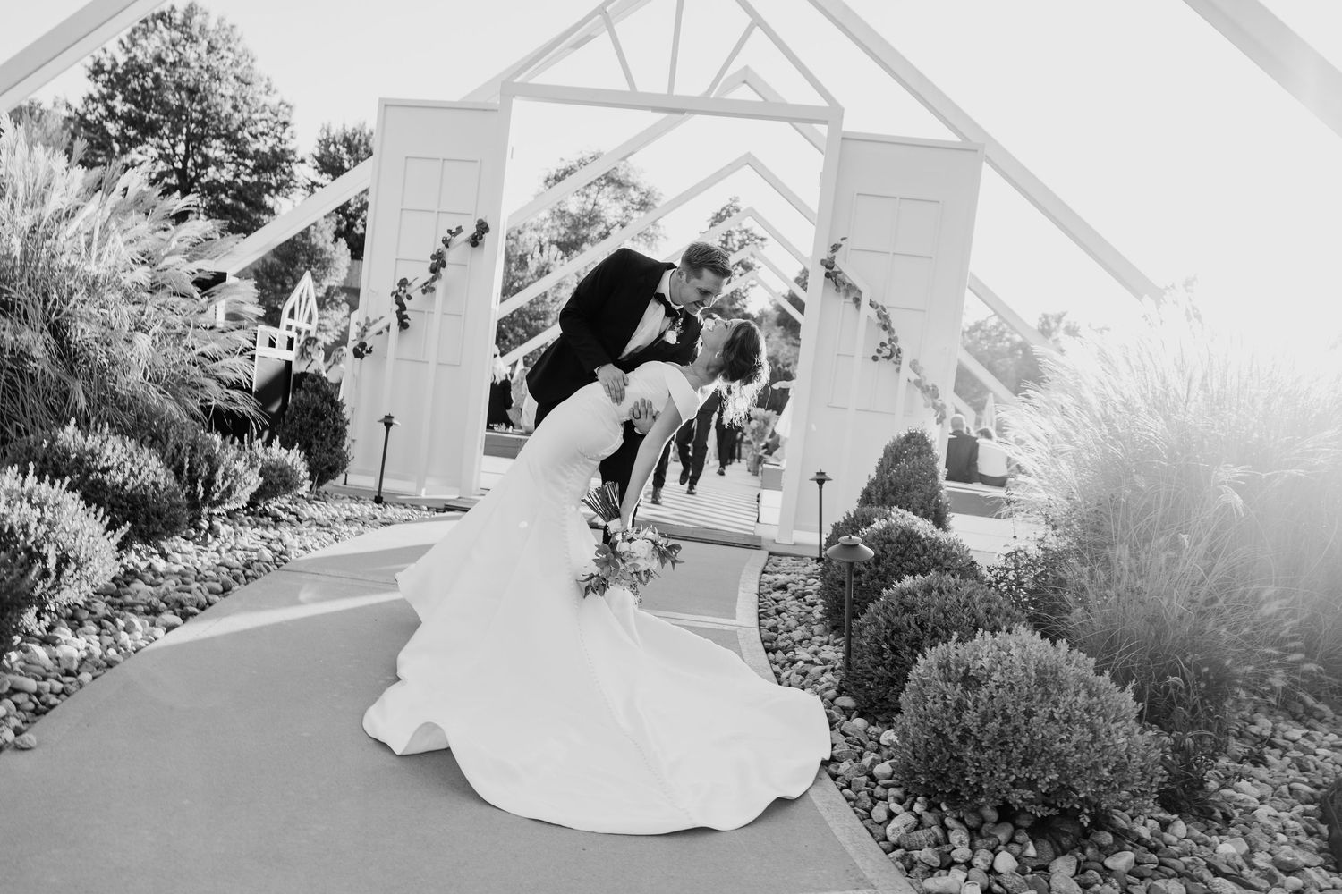 Black and white photo of bride and groom sharing a dip kiss outside wedding chapel.