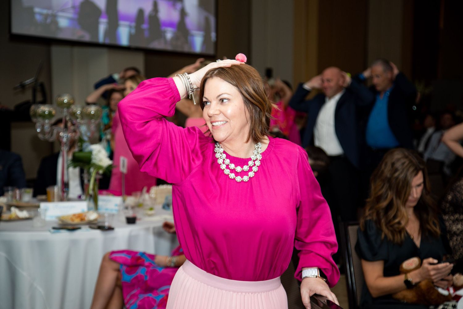 Woman in bright pink blouse and pearl necklace posing at an elegant event.