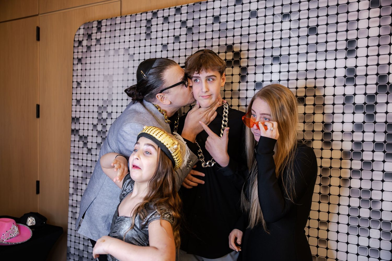 Four people pose playfully at a photo booth with fun props and accessories.