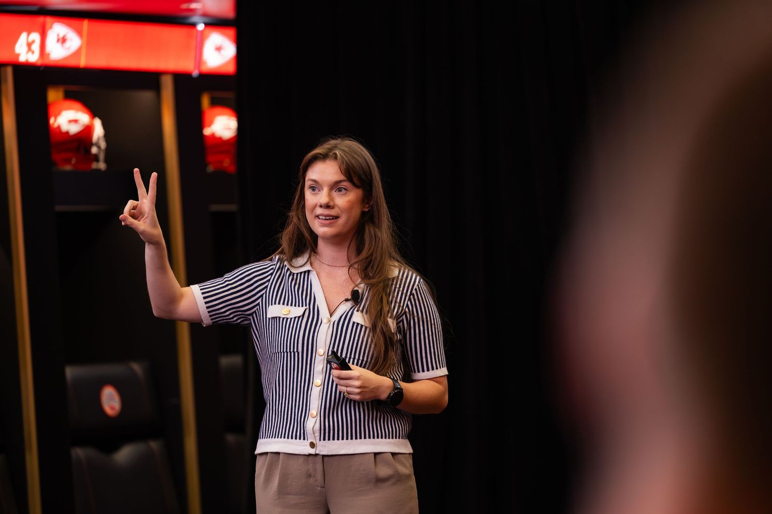 Young woman making a peace sign while presenting at a Kansas City Chiefs venue event.