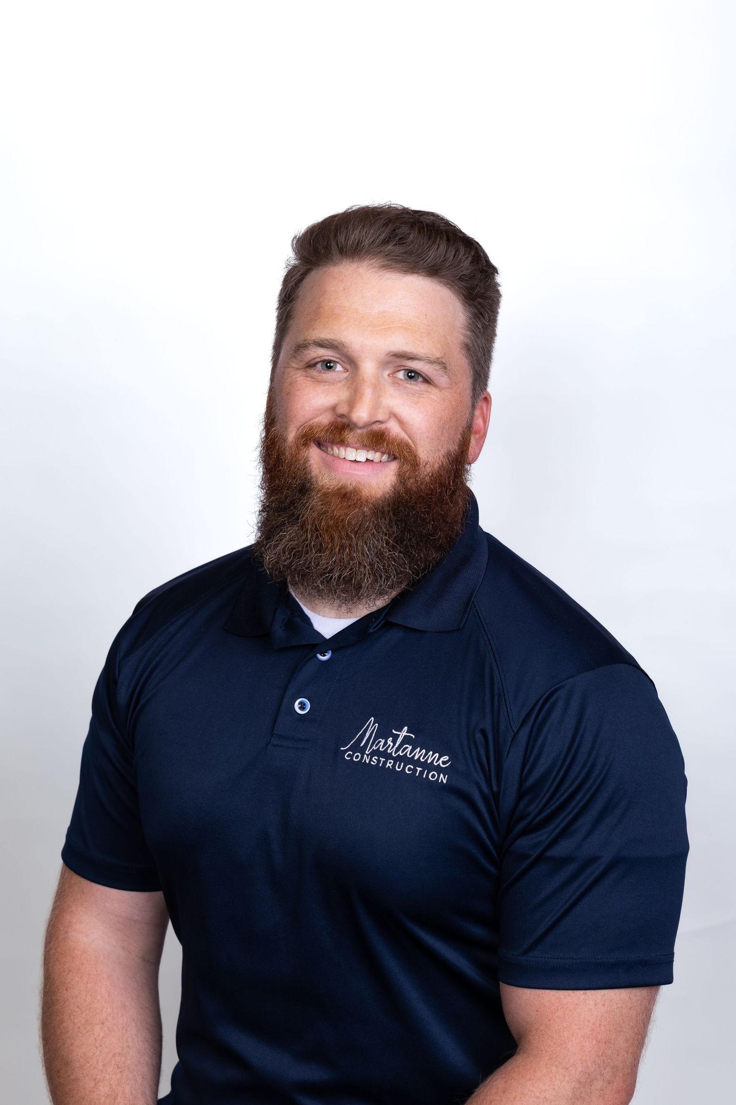 Smiling man with a beard wearing a navy Martanne Construction polo shirt against a white background.
