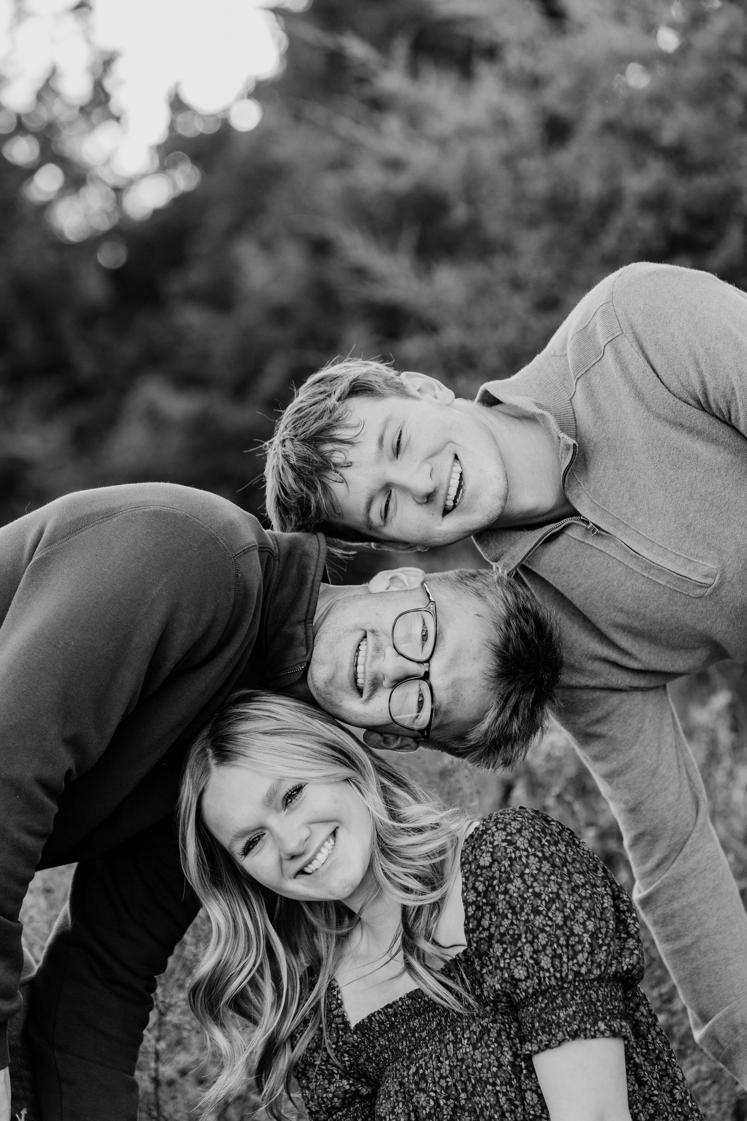 Black and white portrait of three smiling family members stacking heads together outdoors.