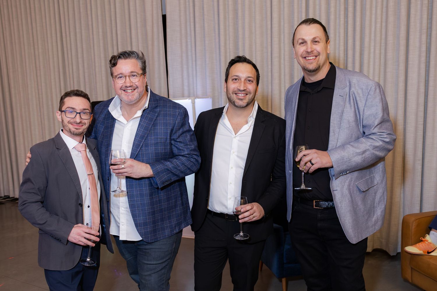 Four men smiling and holding champagne glasses at a formal evening event.