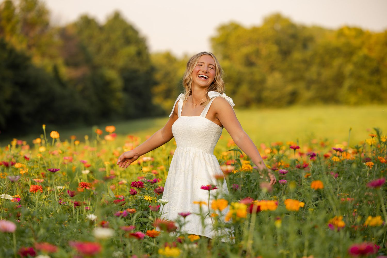 A joyful young woman in a white dress laughs while standing in a vibrant colorful wildflower field.