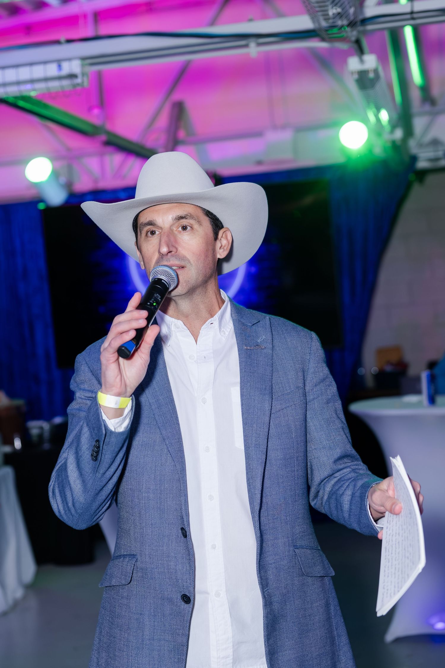 Man in a white cowboy hat speaks into a microphone at a western-themed event.