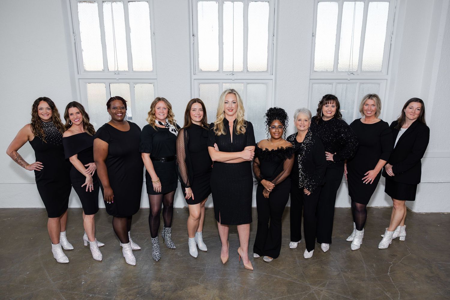 Group of women in black outfits posing together in a bright white studio setting for a professional photo.