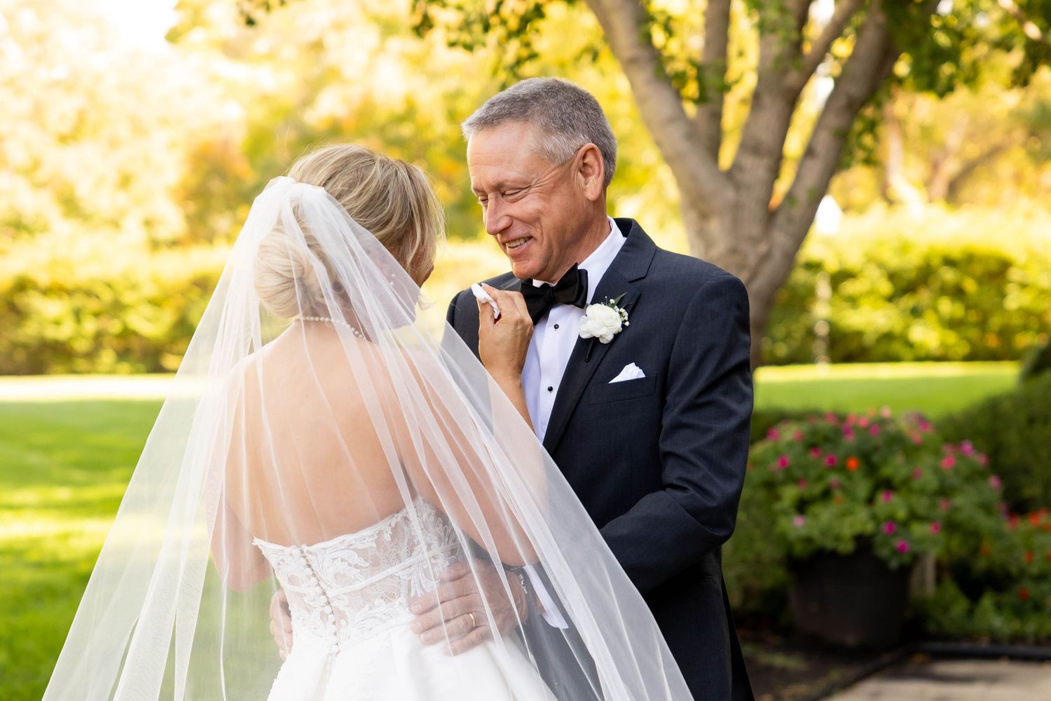 Emotional father in tuxedo smiling at his daughter the bride during an outdoor first look moment.