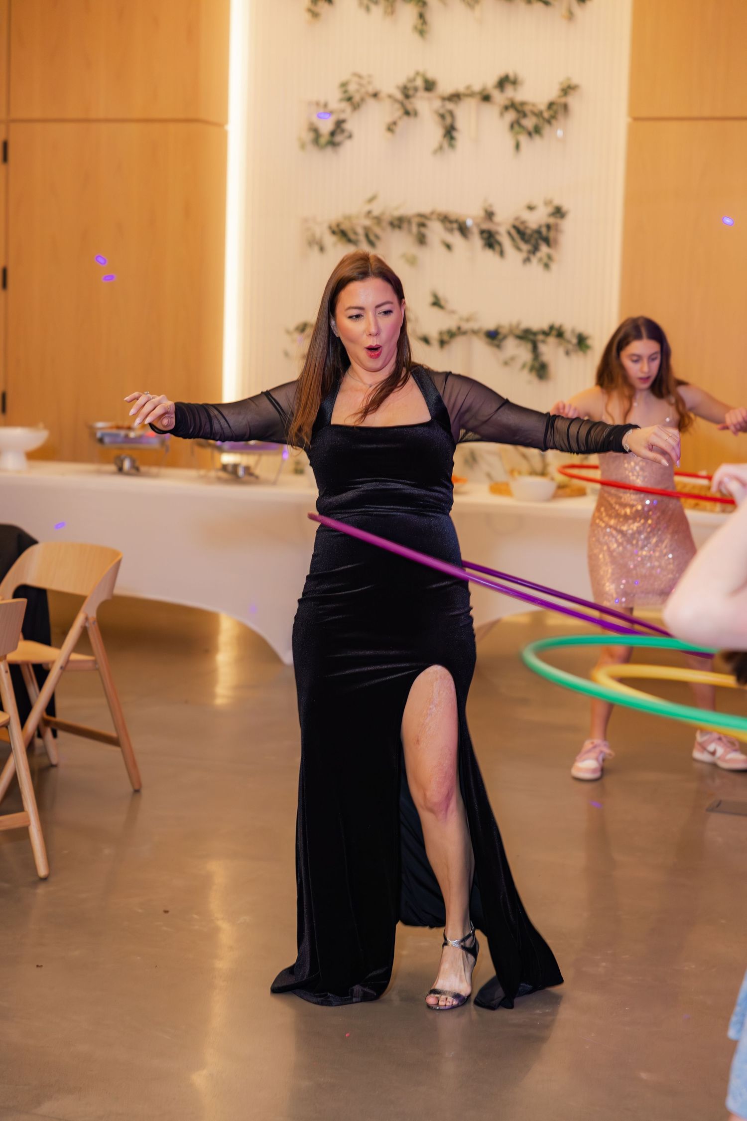 Woman in black velvet gown hula hooping at a festive indoor celebration.