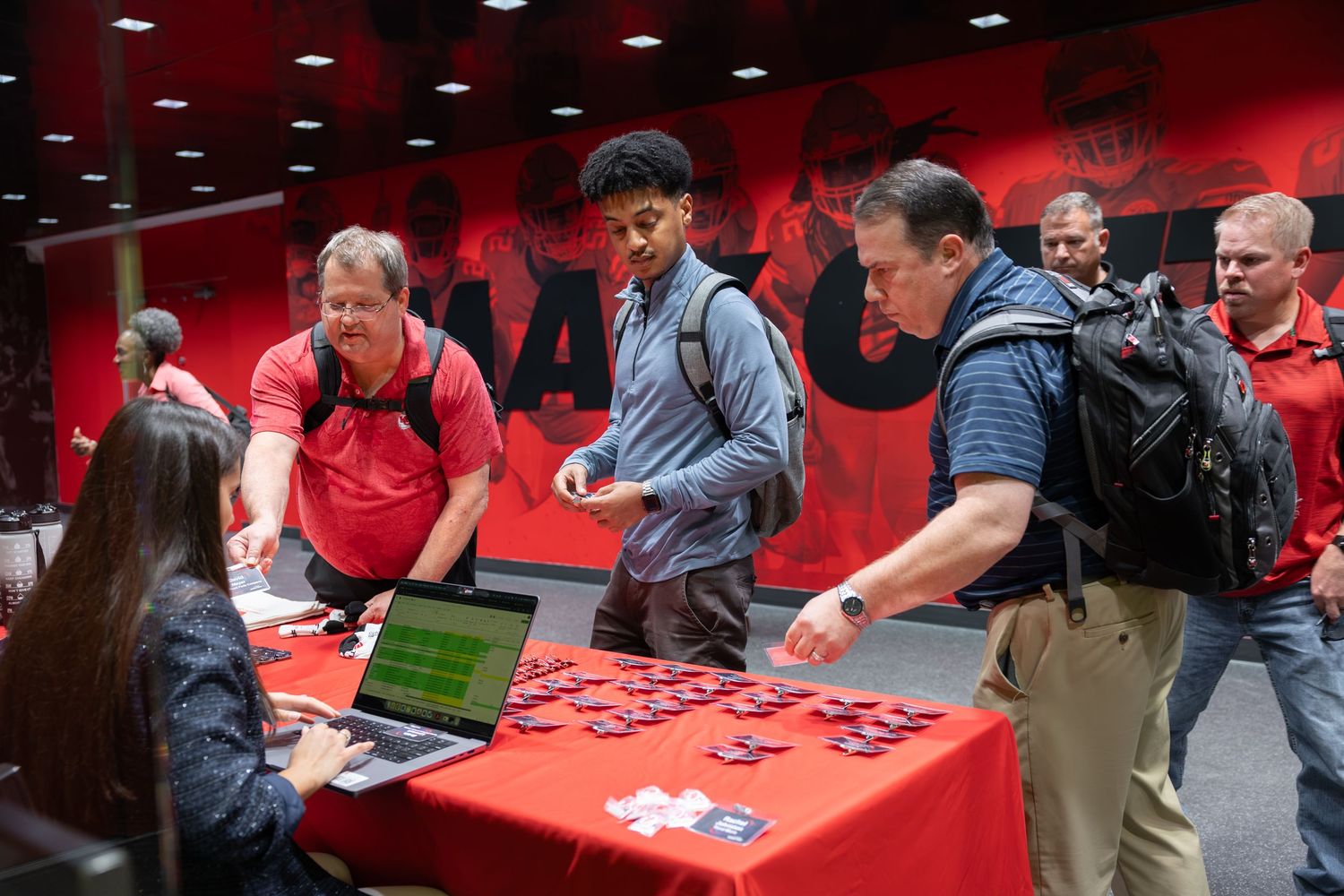 People checking in at a registration table inside a Kansas City Chiefs facility with red decor.
