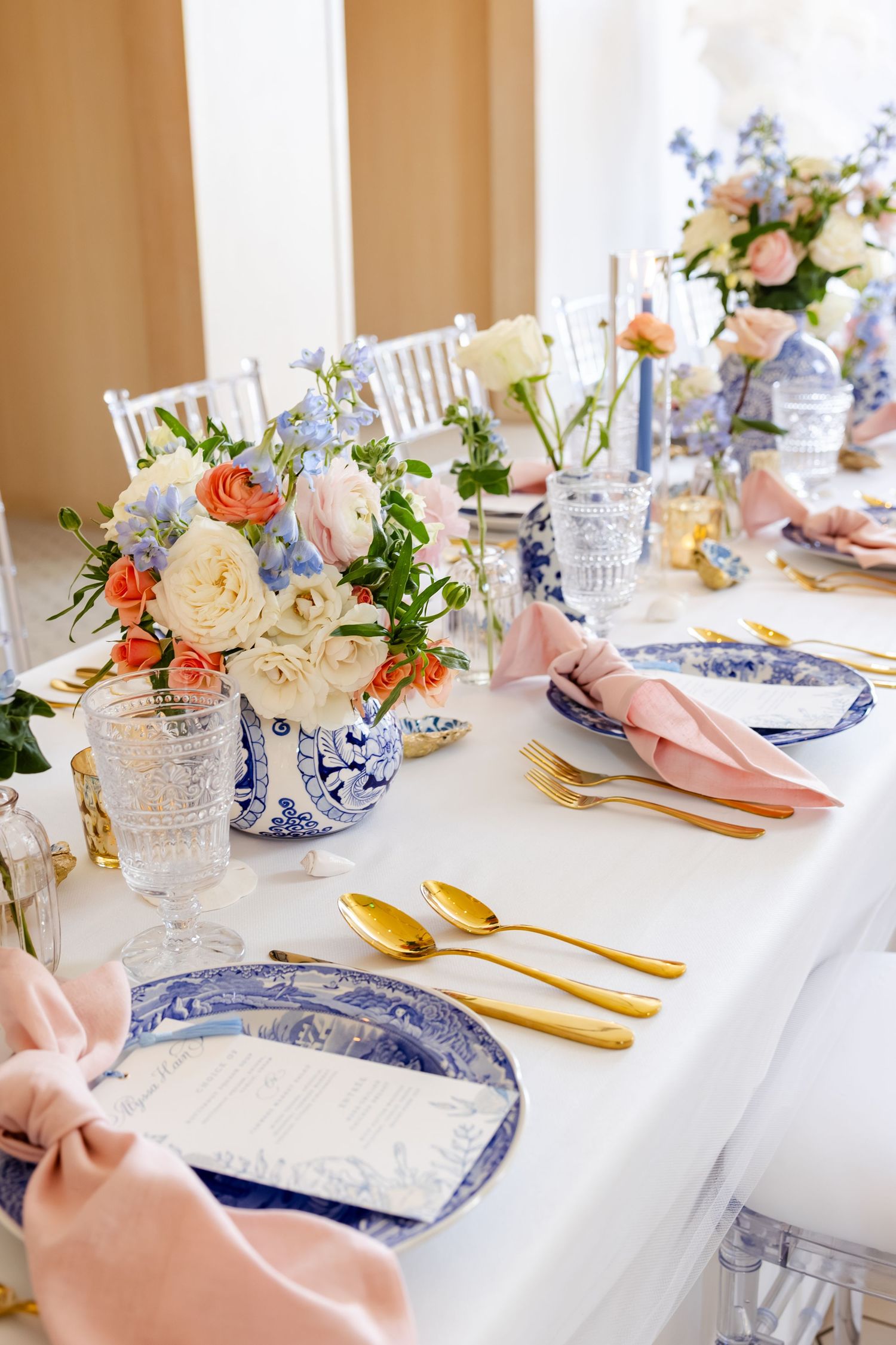 Elegant table setting with blue and white plates, gold cutlery, and floral centerpiece.